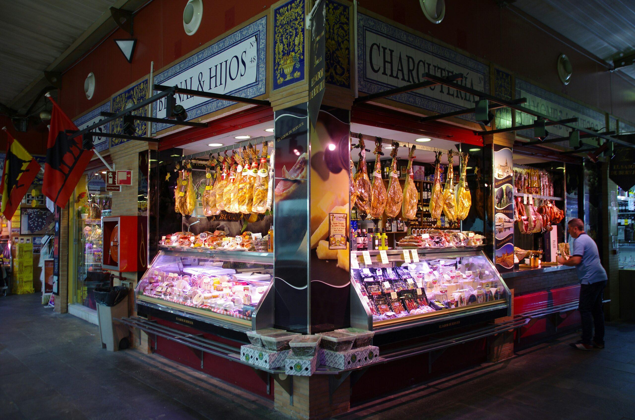 Charcutería tradicional española con jamones ibéricos colgados y vitrinas refrigeradas con productos de calidad