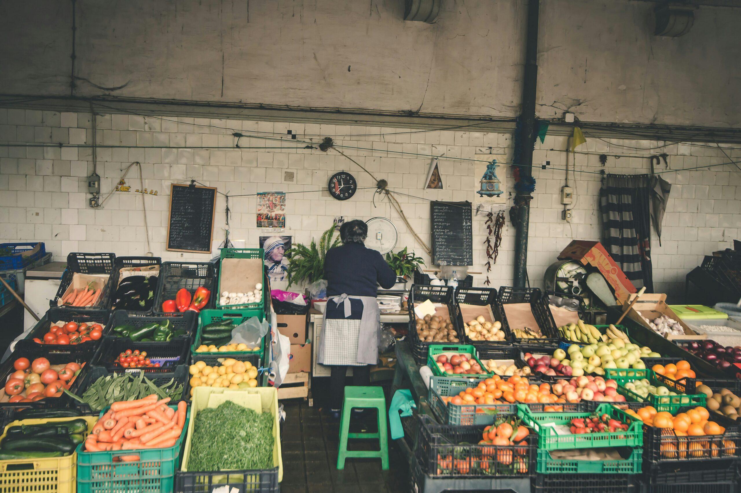 Un vendedor de frutas y verduras frescas en un mercado cubierto tradicional con puestos coloridos y paredes de azulejo blanco