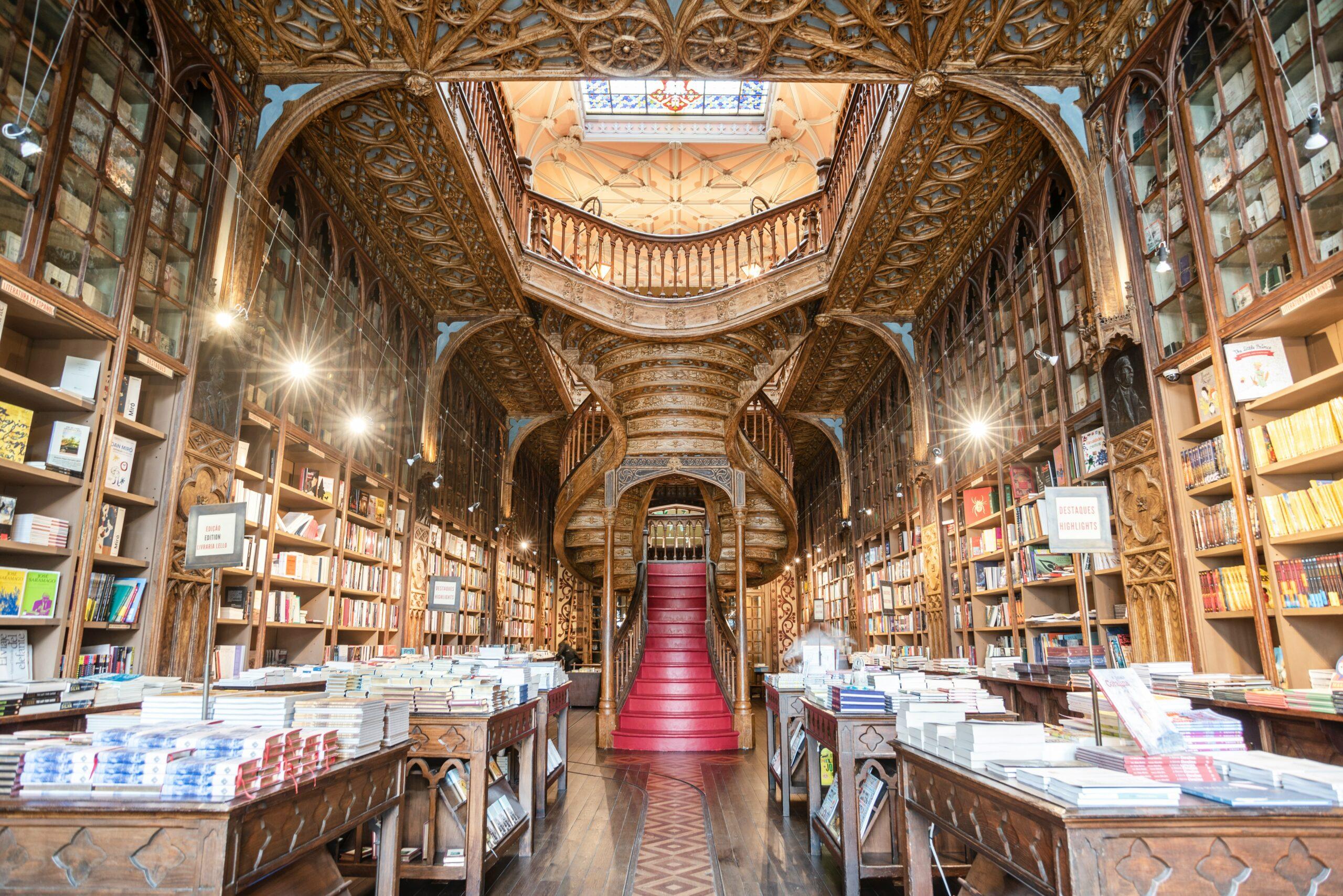 Interior ornamentado de una librería histórica con techo esculpido, estanterías de madera y escalera central en rojo