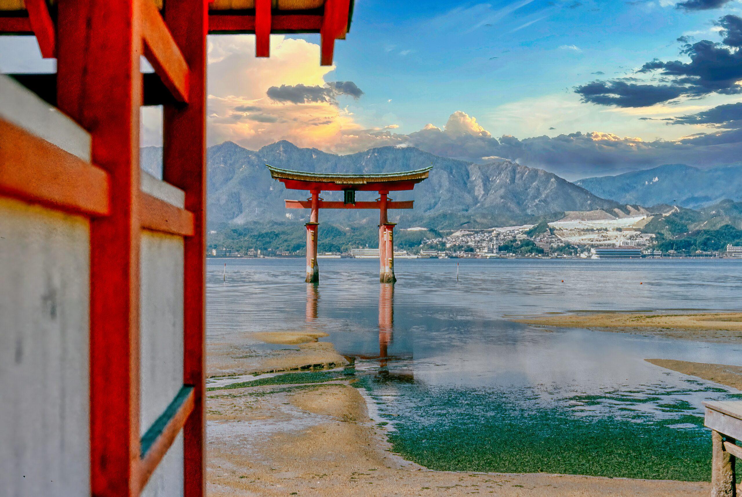 Un torii rosso tradizionale emerge dalle acque basse di fronte alle montagne, con un tempio sullo sfondo