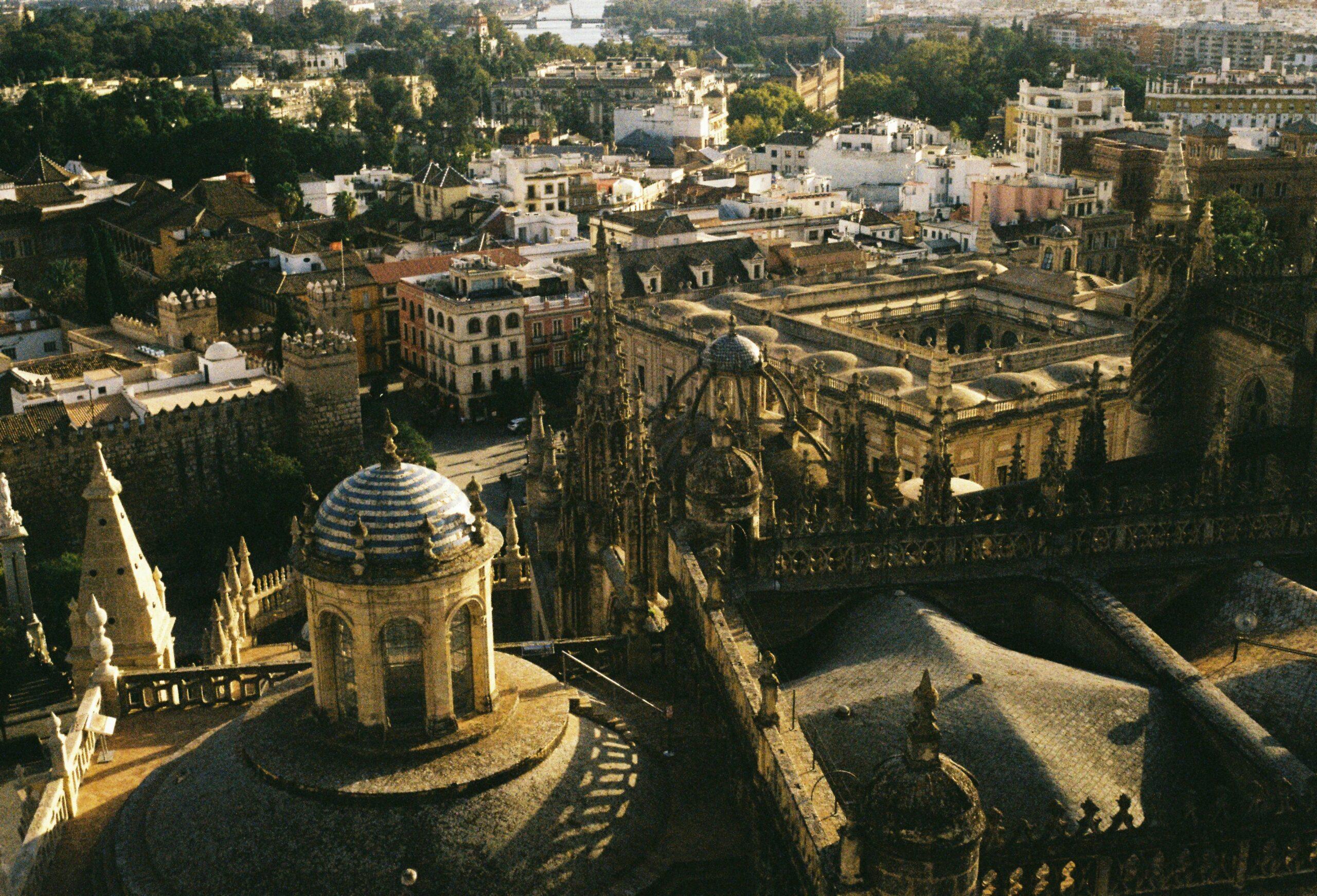 Vista aérea de la Catedral de Sevilla con sus tejados dorados, rodeada de edificios históricos y jardines andaluces