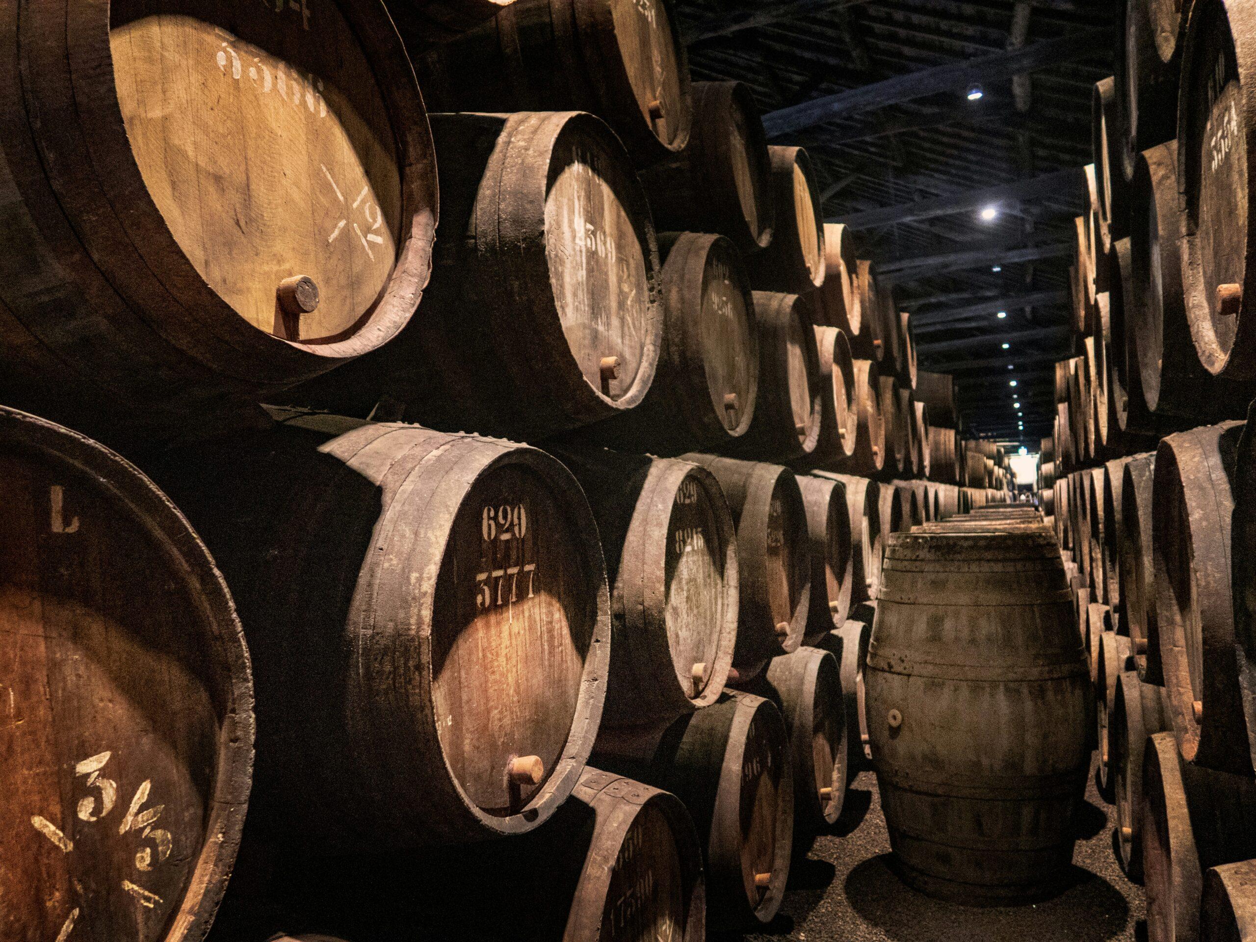 Filas de barricas de vino apiladas en una bodega subterránea iluminada, con números grabados en la madera