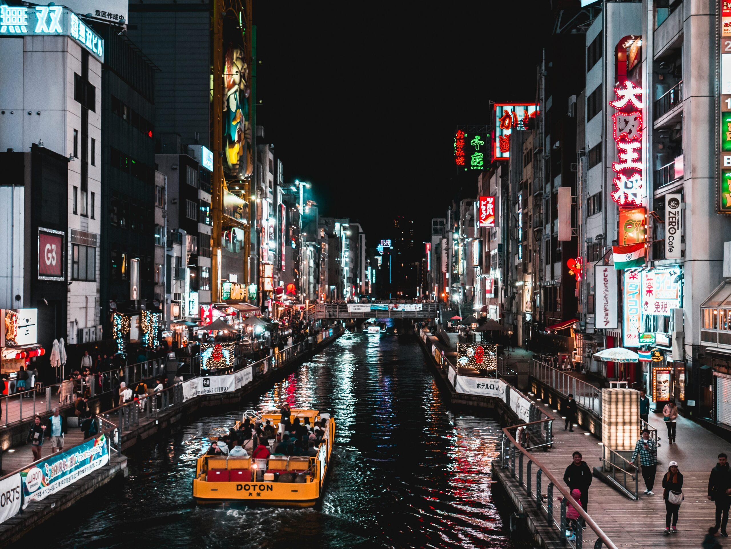 Un canale illuminato di notte in una vivace via commerciale giapponese con insegne al neon e battello turistico giallo