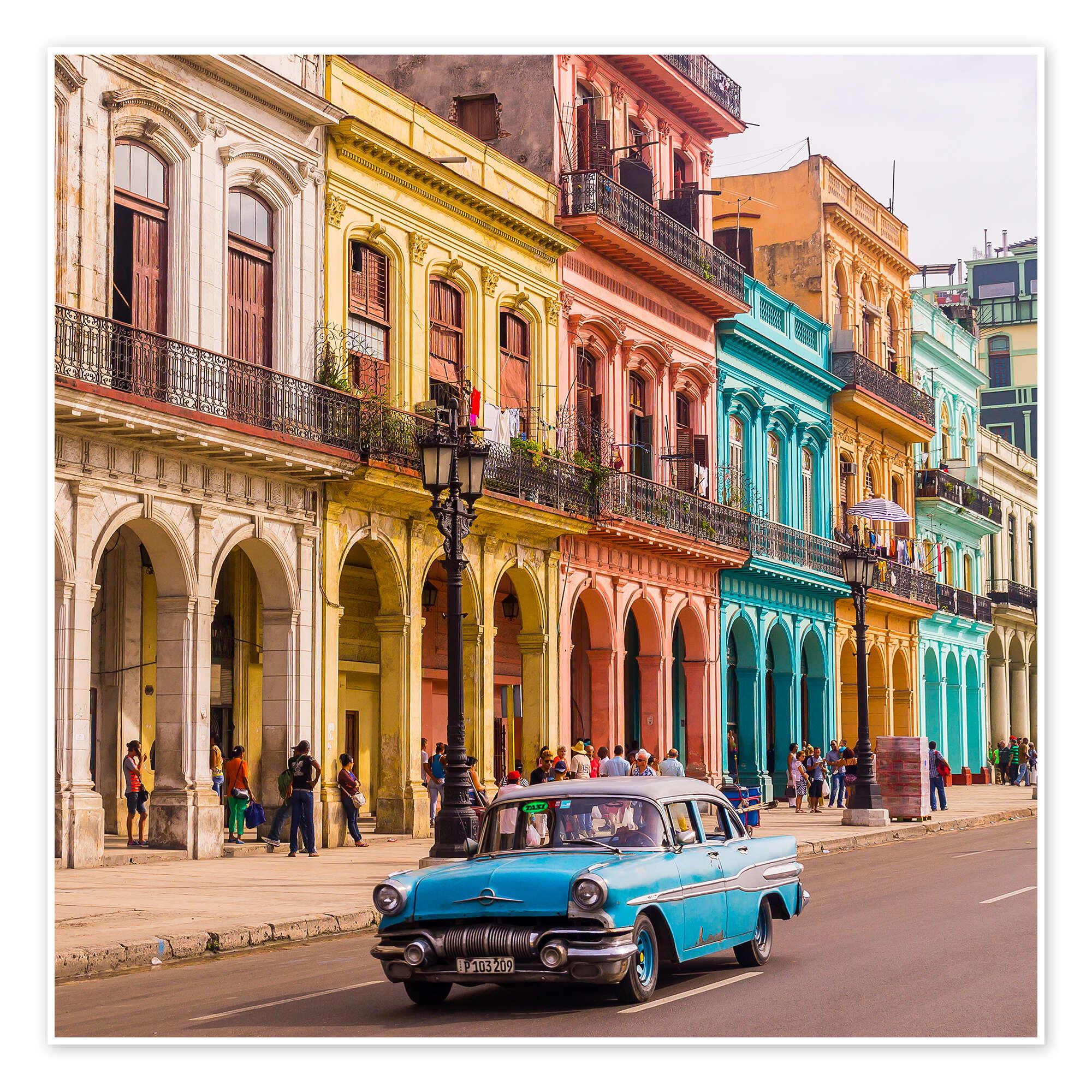 Un’auto americana blu d’epoca percorre una strada acciottolata animata davanti a edifici coloniali dai colori vivaci