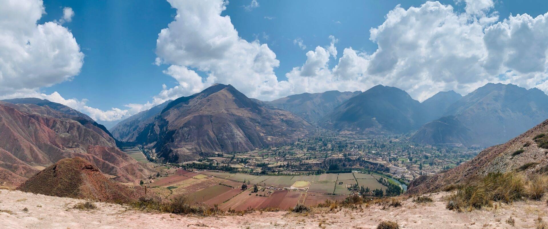 Valle andino con montañas escarpadas, campos cultivados en terrazas, río serpenteante y aldeas dispersas bajo cielo nublado
