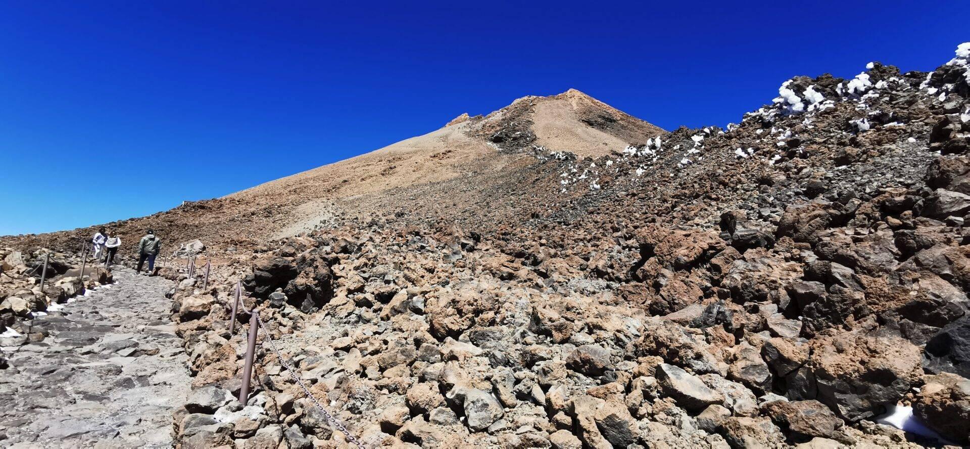 Escursionisti che salgono un sentiero roccioso verso una cima arida sotto un cielo azzurro limpido