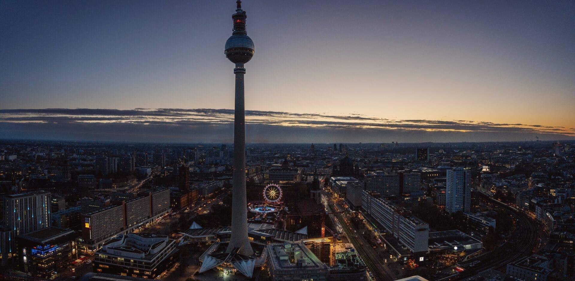 Vista panoramica al tramonto di una grande torre televisiva che domina una metropoli tedesca con una grande ruota panoramica illuminata