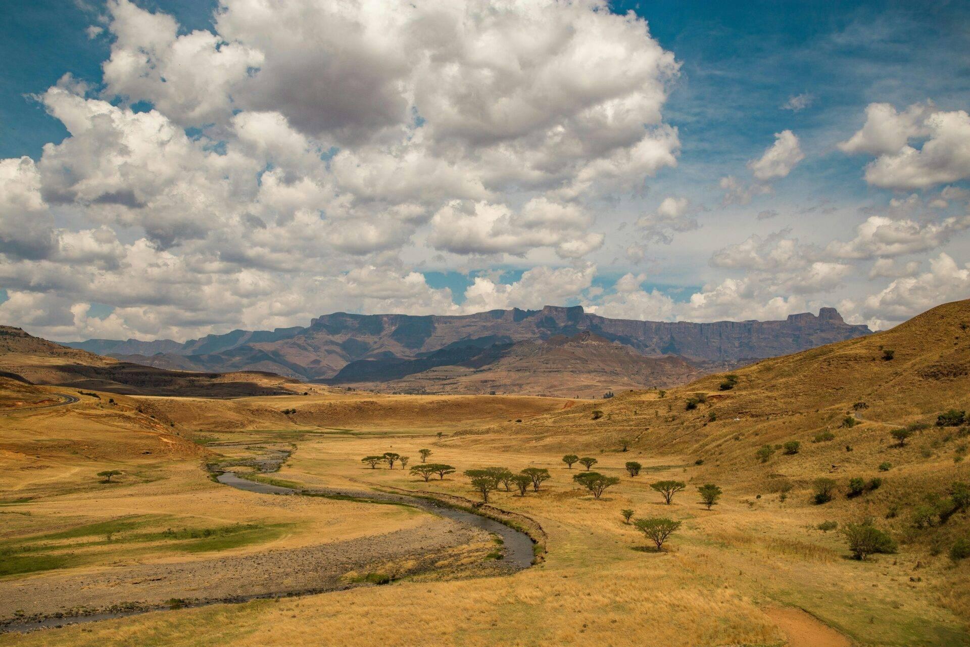 Vallée fluviale avec montagnes escarpées, savane aride parsemée d’acacias et ciel nuageux spectaculaire