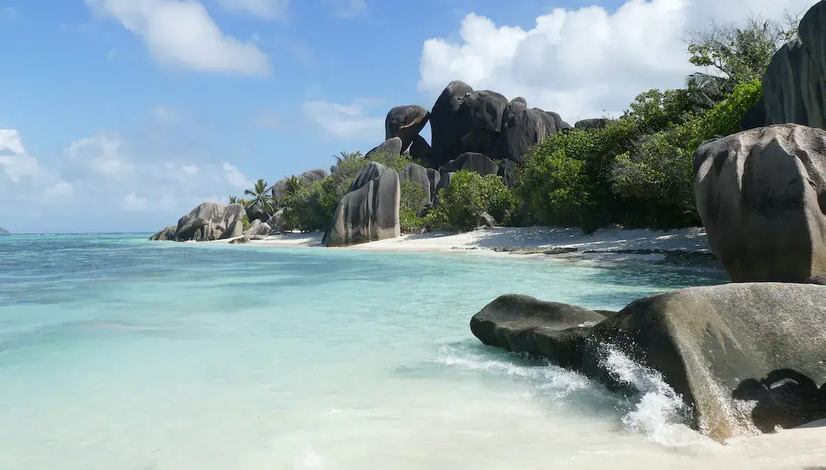 Playa tropical con imponentes rocas graníticas, arena blanca y agua turquesa cristalina bajo un cielo despejado