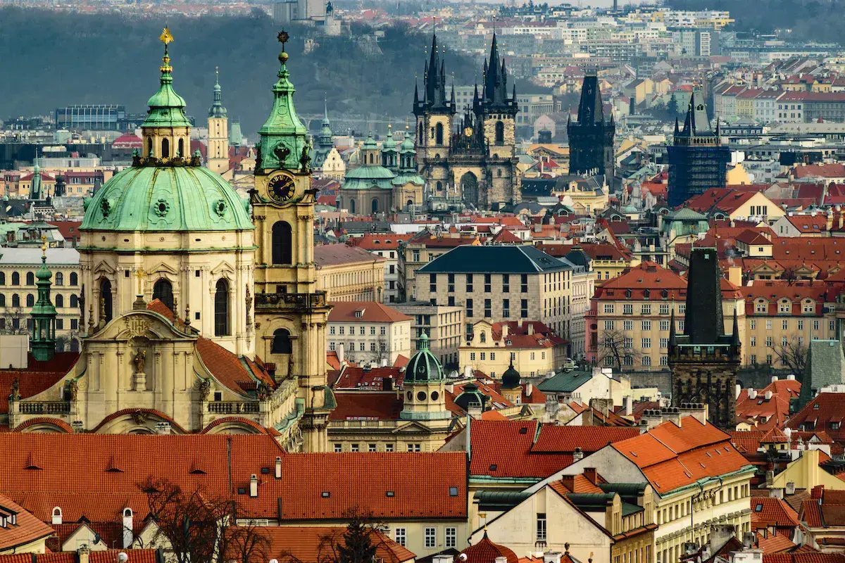 Vista panorámica de una ciudad europea con iglesias de cúpulas verdes y torres góticas negras que dominan la arquitectura histórica