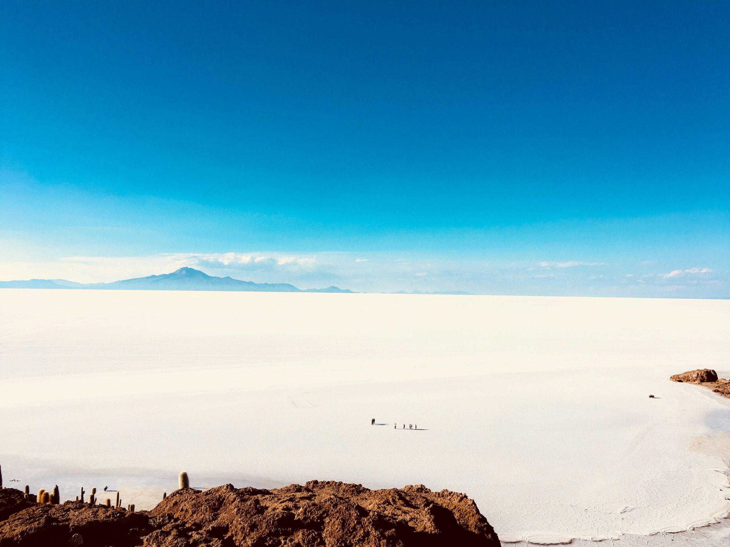 Blick auf den Salar de Uyuni vom Boden aus, weiße hexagonale Salzplatten so weit das Auge reicht unter dem blauen Himmel des bolivianischen Altiplanos