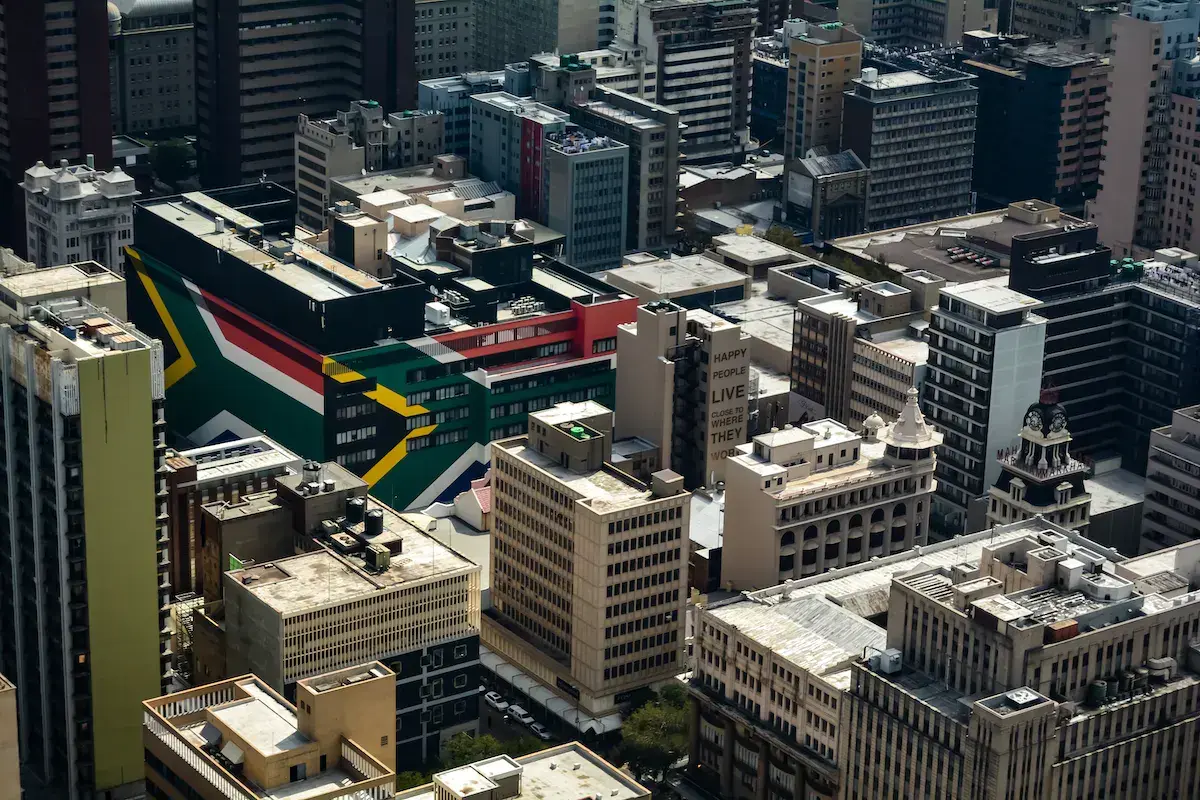 Vista aérea de un barrio urbano con un edificio en los colores de la bandera sudafricana entre rascacielos