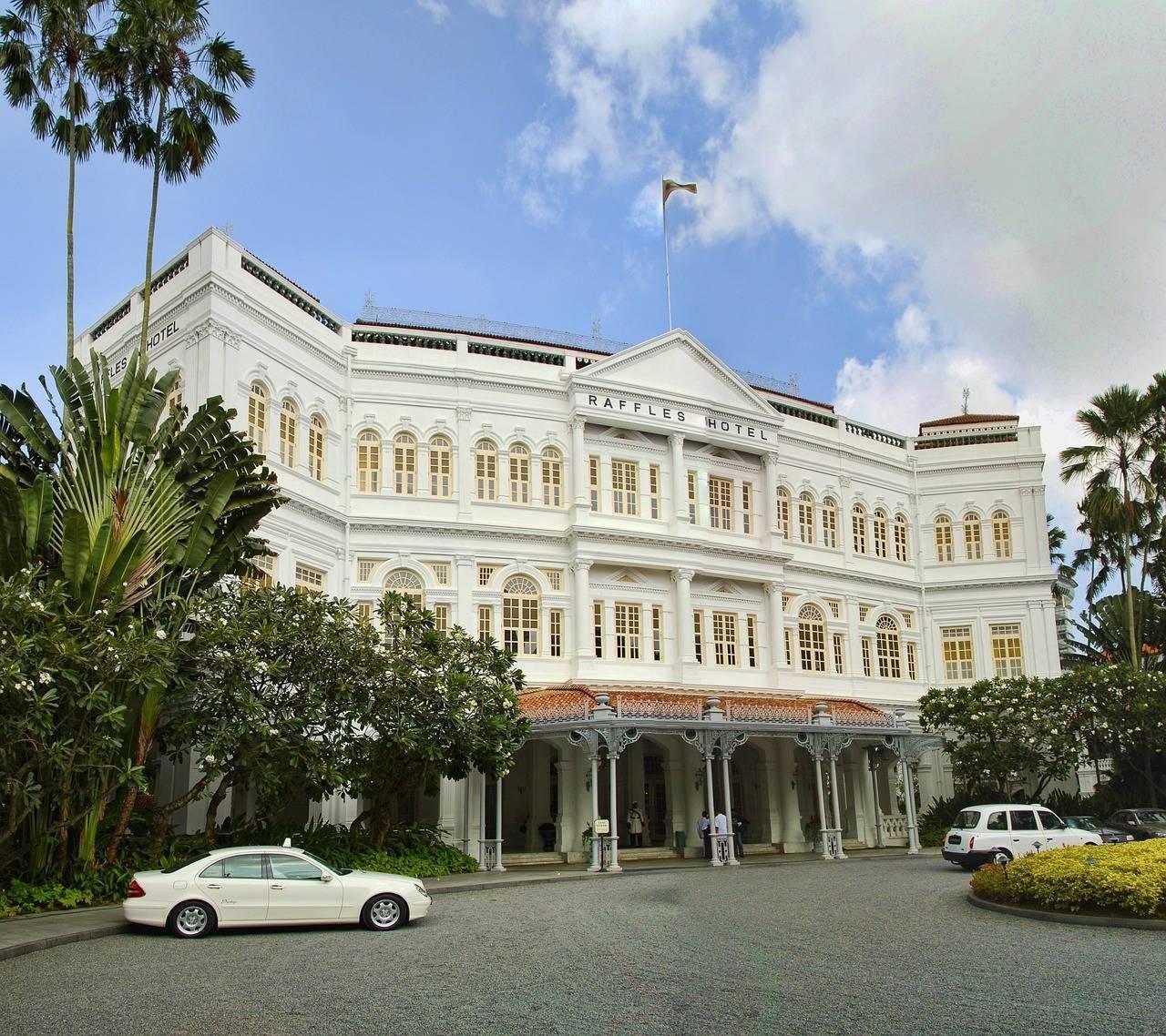 Ein majestätisches weißes Kolonialhotel mit Säulen, umgeben von Tropenpalmen und parkenden Autos davor