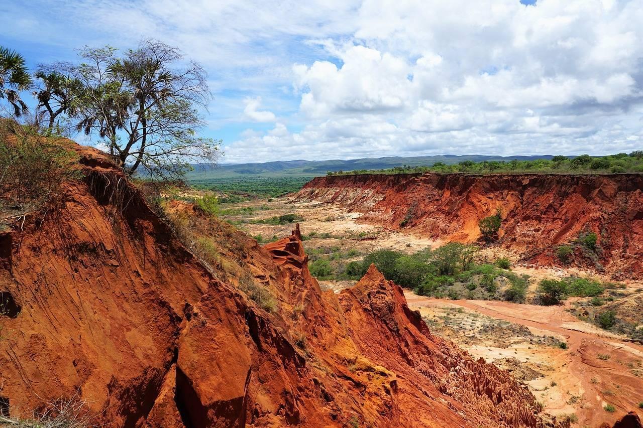 Cava di laterite con formazioni rocciose rosse che dominano una valle verdeggiante sotto cielo nuvoloso