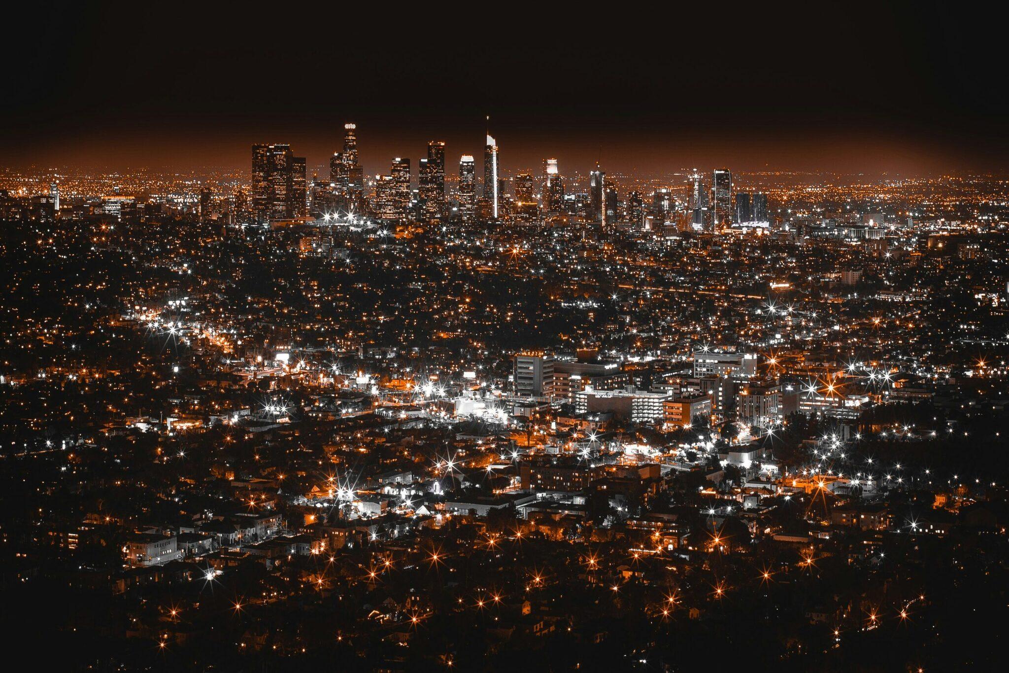 Vista nocturna de una gran metrópoli con rascacielos iluminados en el centro y barrios residenciales que brillan hasta el horizonte