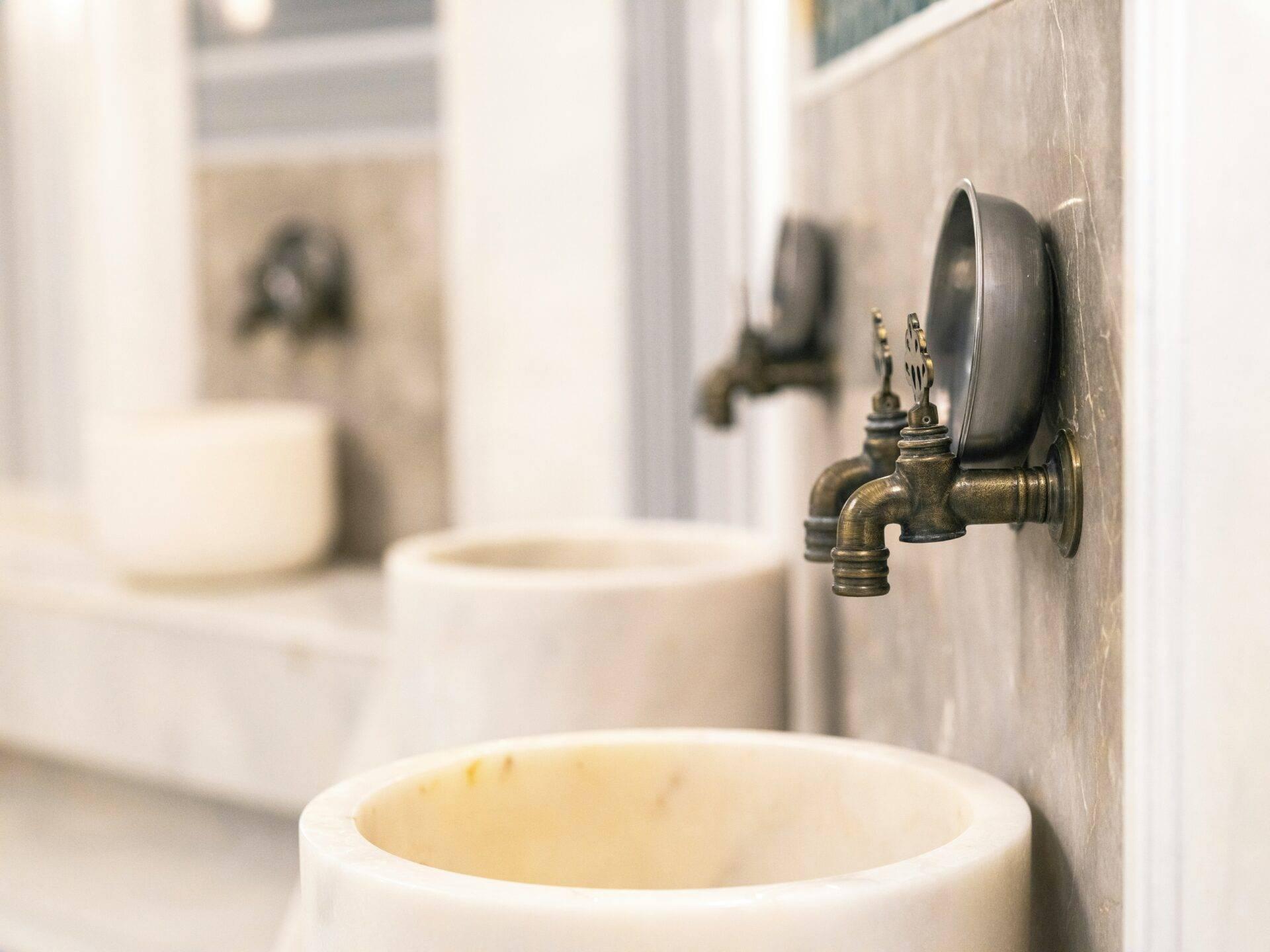 Detalle de un grifo de latón antiguo en una sala de baño tradicional con azulejos beige