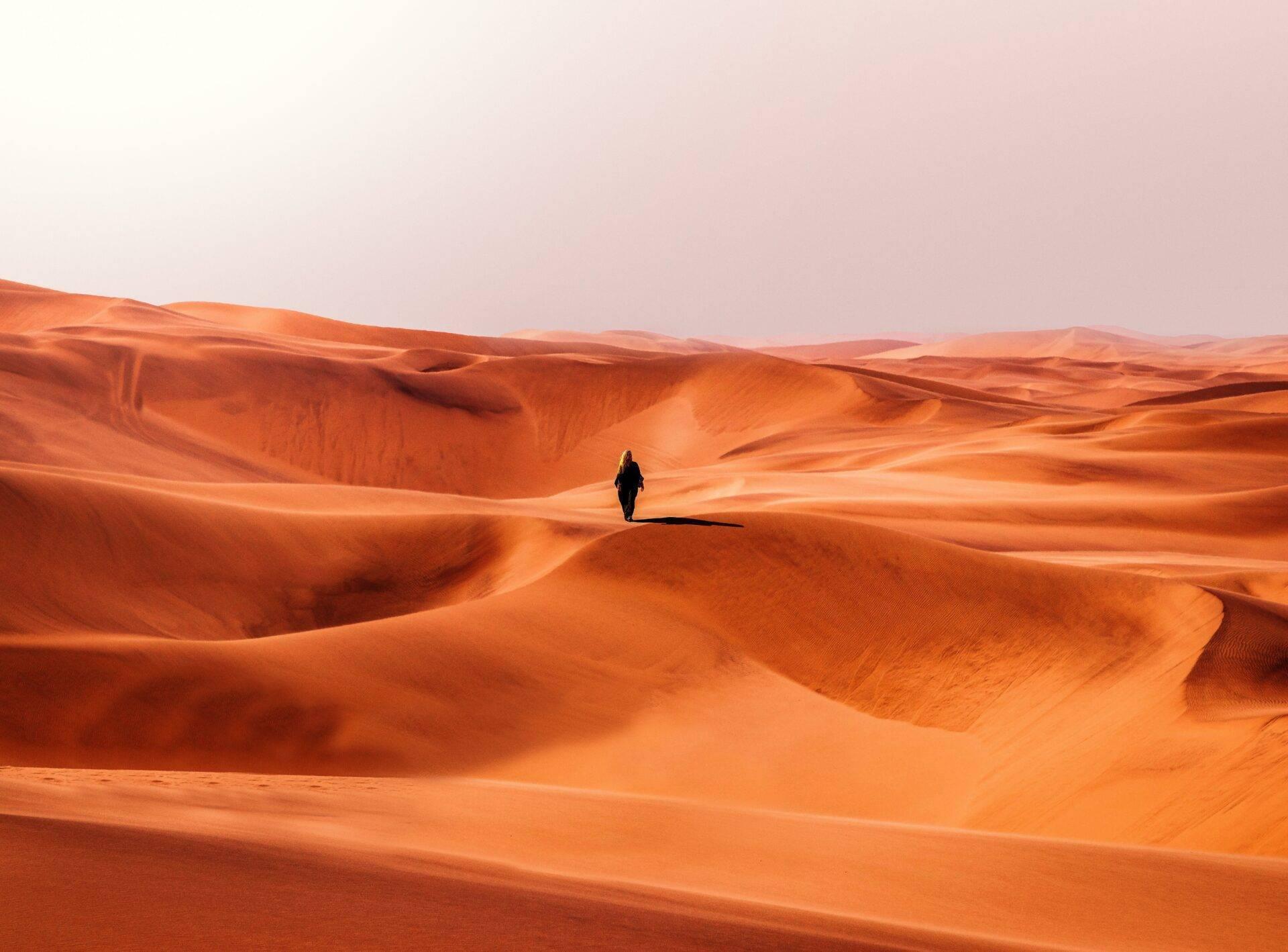 Ein einsamer Reisender wandert durch orangefarbene Sanddünen unter klarem Himmel