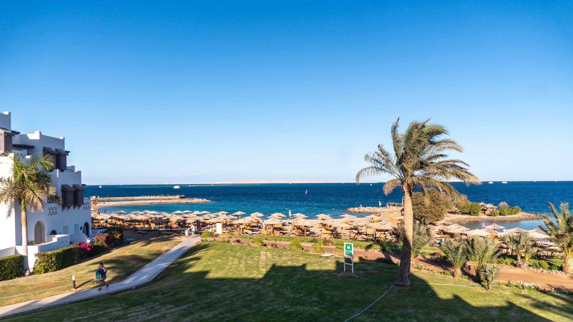 Vista aerea di una stazione balneare con spiaggia di sabbia, palme e architettura bianca affacciata sul mare turchese