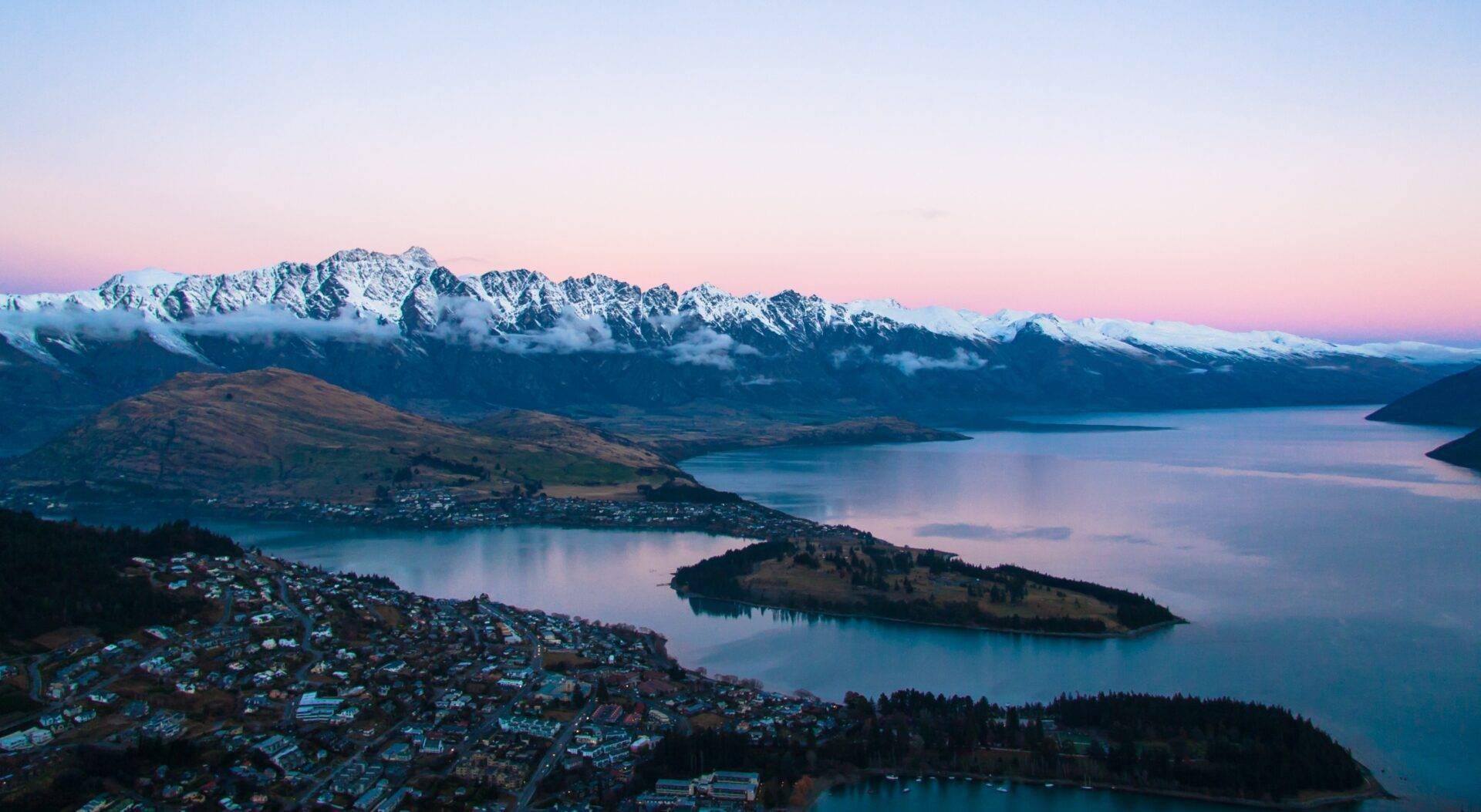 Vista aerea di una città costiera con lago alpino, montagne innevate e penisole boscose al crepuscolo