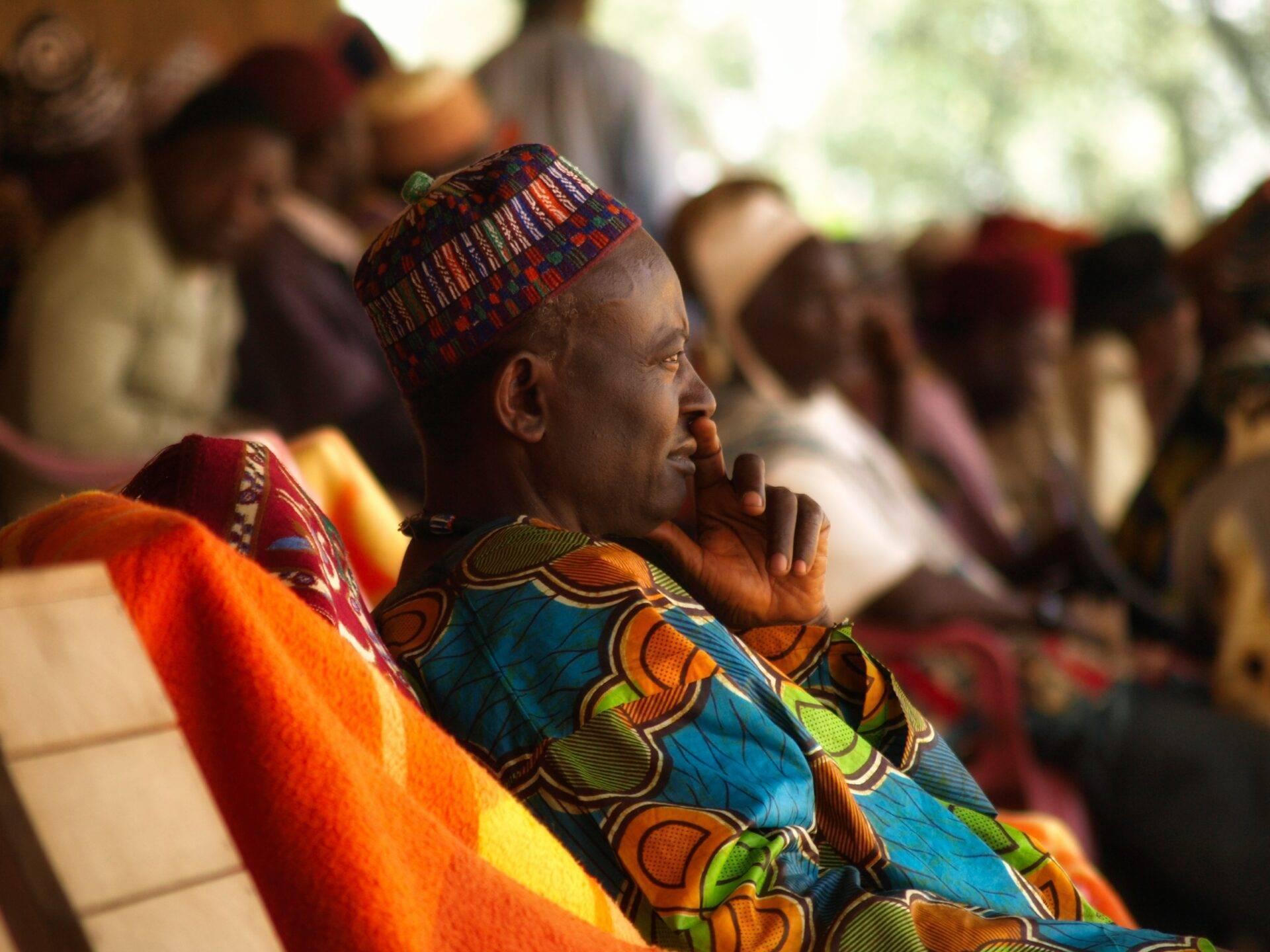 Un hombre vestido con telas tradicionales de colores asiste a una ceremonia cultural africana junto a otros participantes