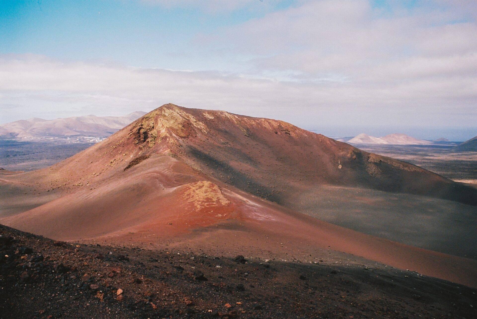 Vulcano dai versanti rossastri e neri che domina un paesaggio arido di montagna desertica sotto un cielo limpido