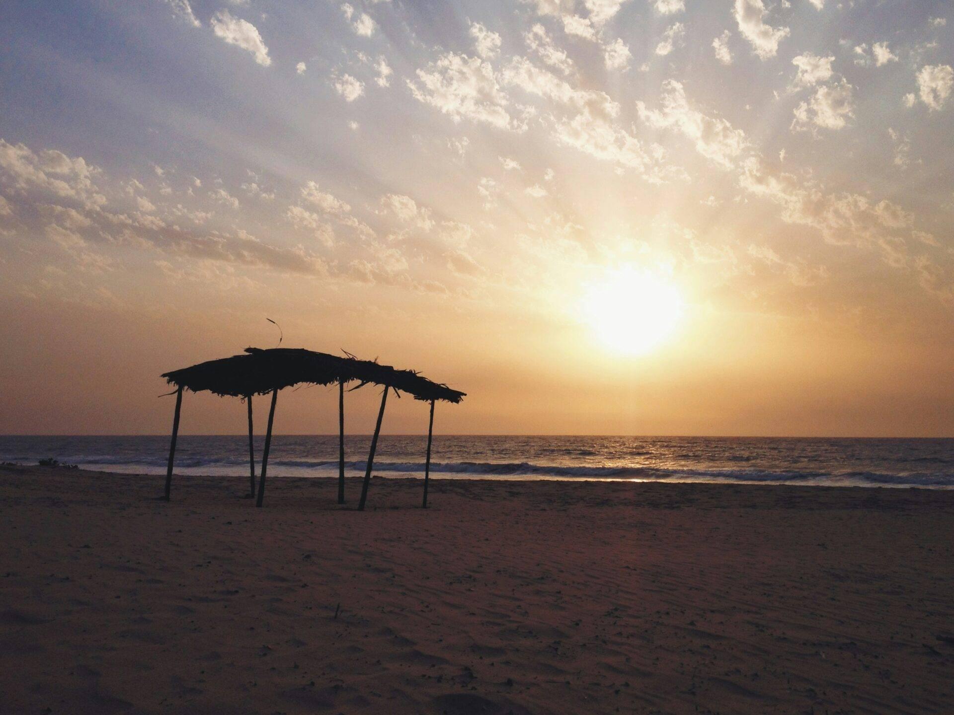 Un abri en paille sur une plage de sable face à l’océan au coucher du soleil