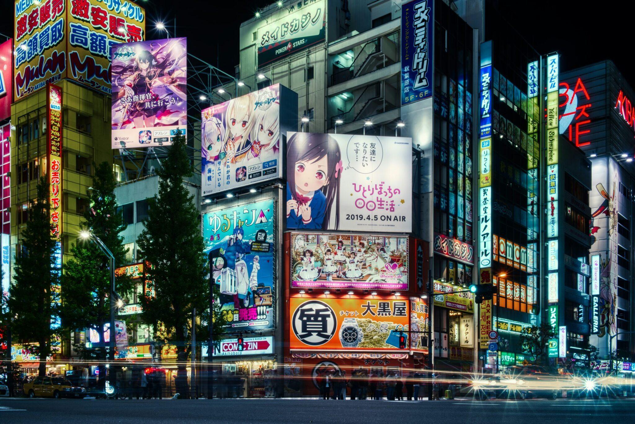 Una calle comercial animada de noche con edificios iluminados, carteles publicitarios de colores y posters de anime japonés