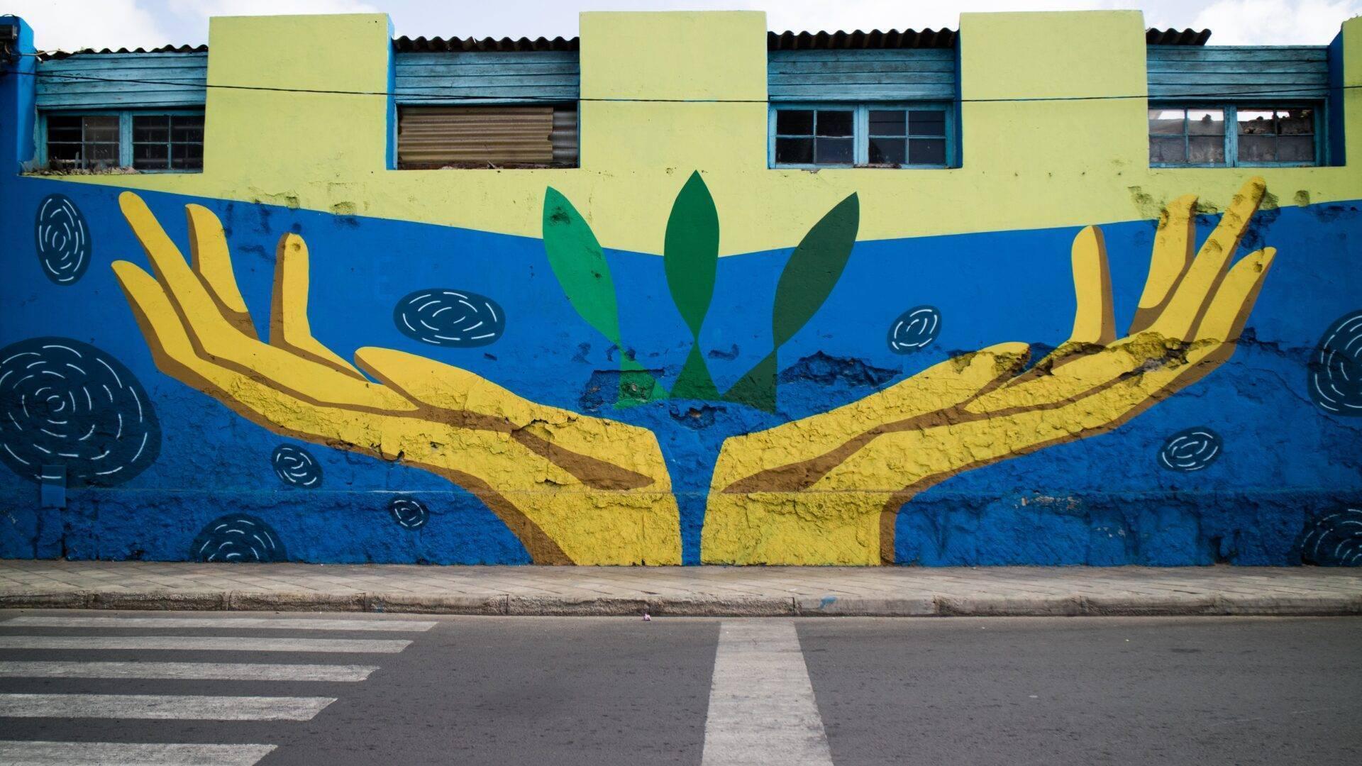 Colourful mural depicting yellow hands cradling a green plant on a blue background
