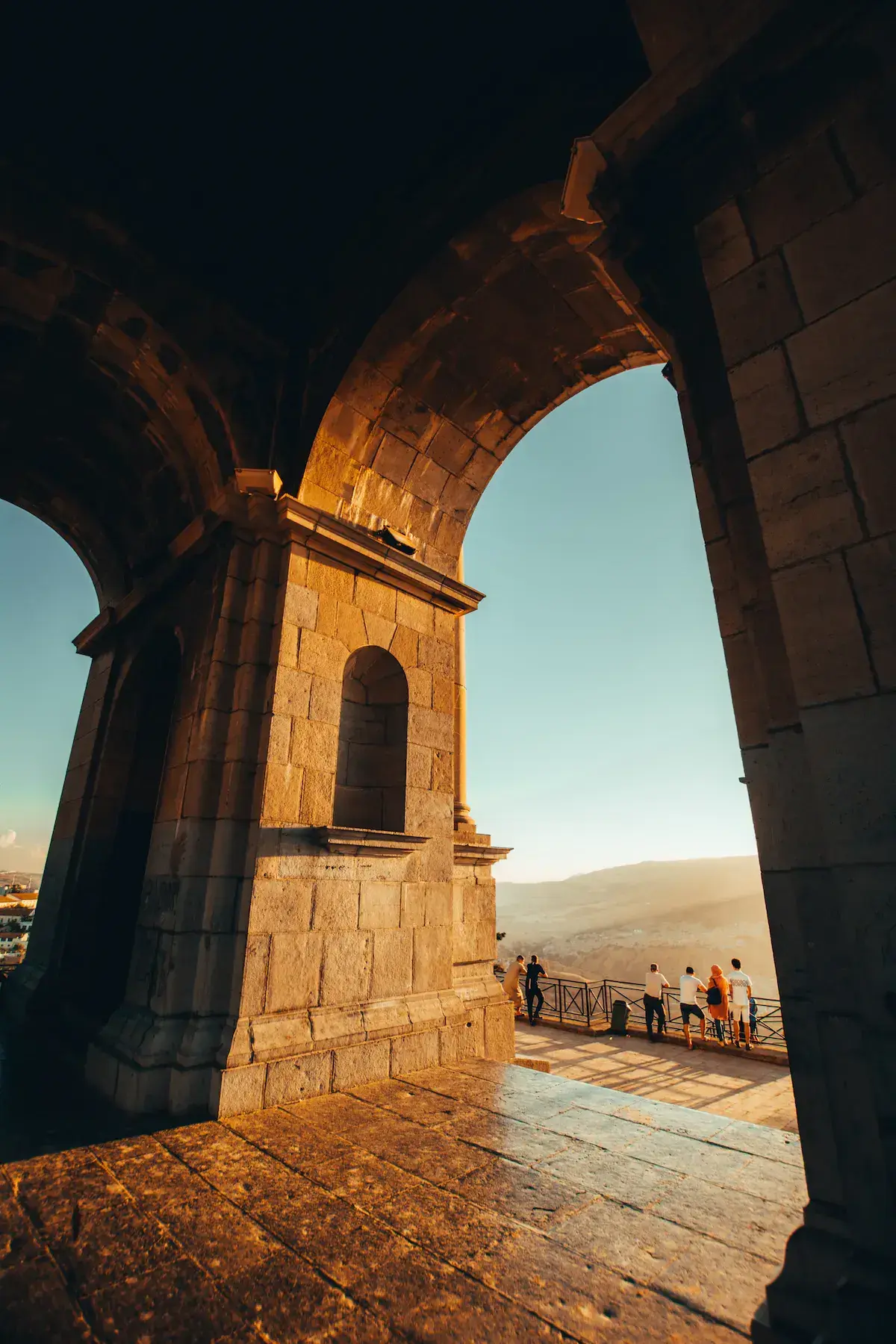Ruinas de piedra con arcos majestuosos que se asoman a un paisaje montañoso desértico al atardecer
