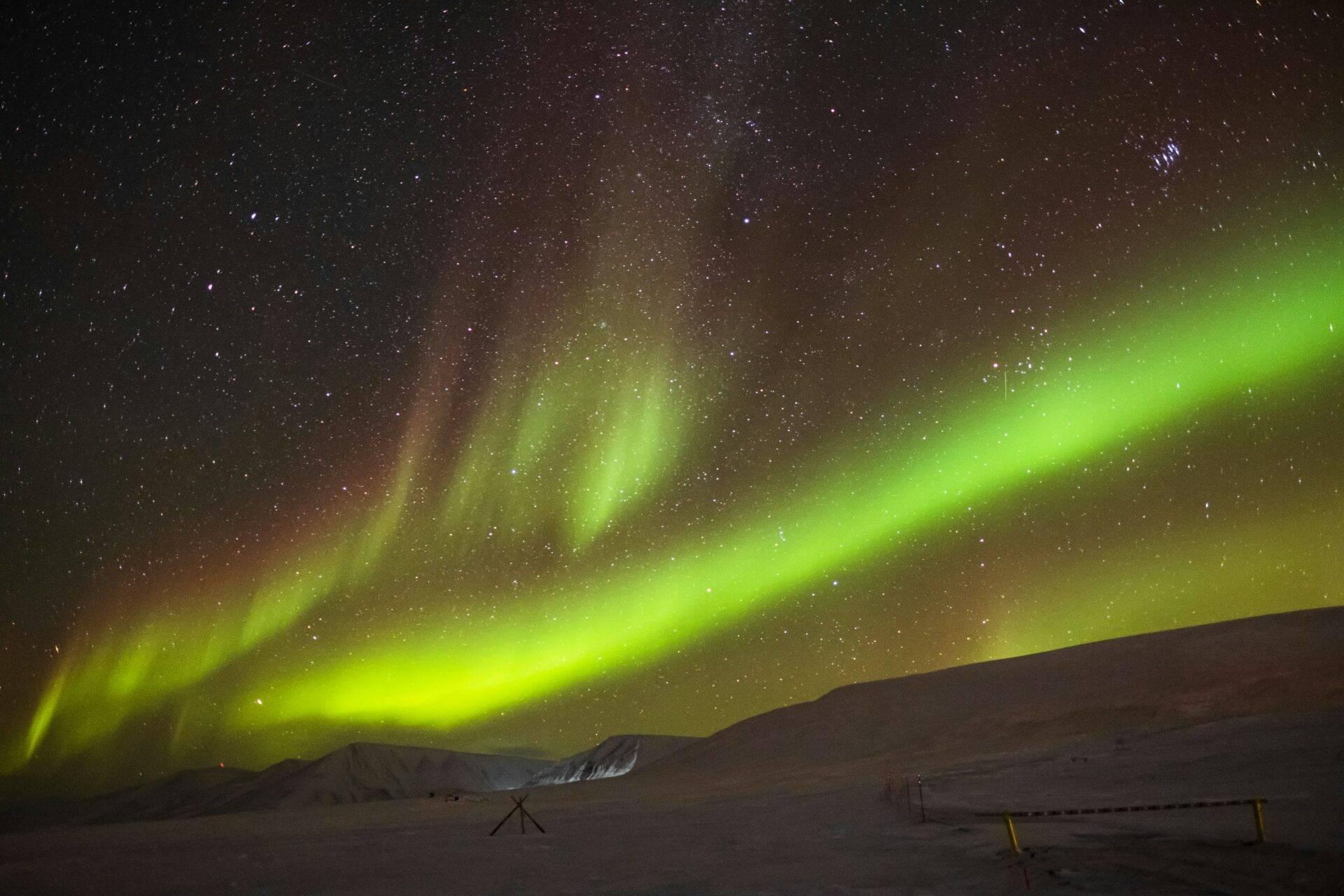 Auroras boreales verdes danzando sobre un paisaje ártico nevado salpicado de equipamientos
