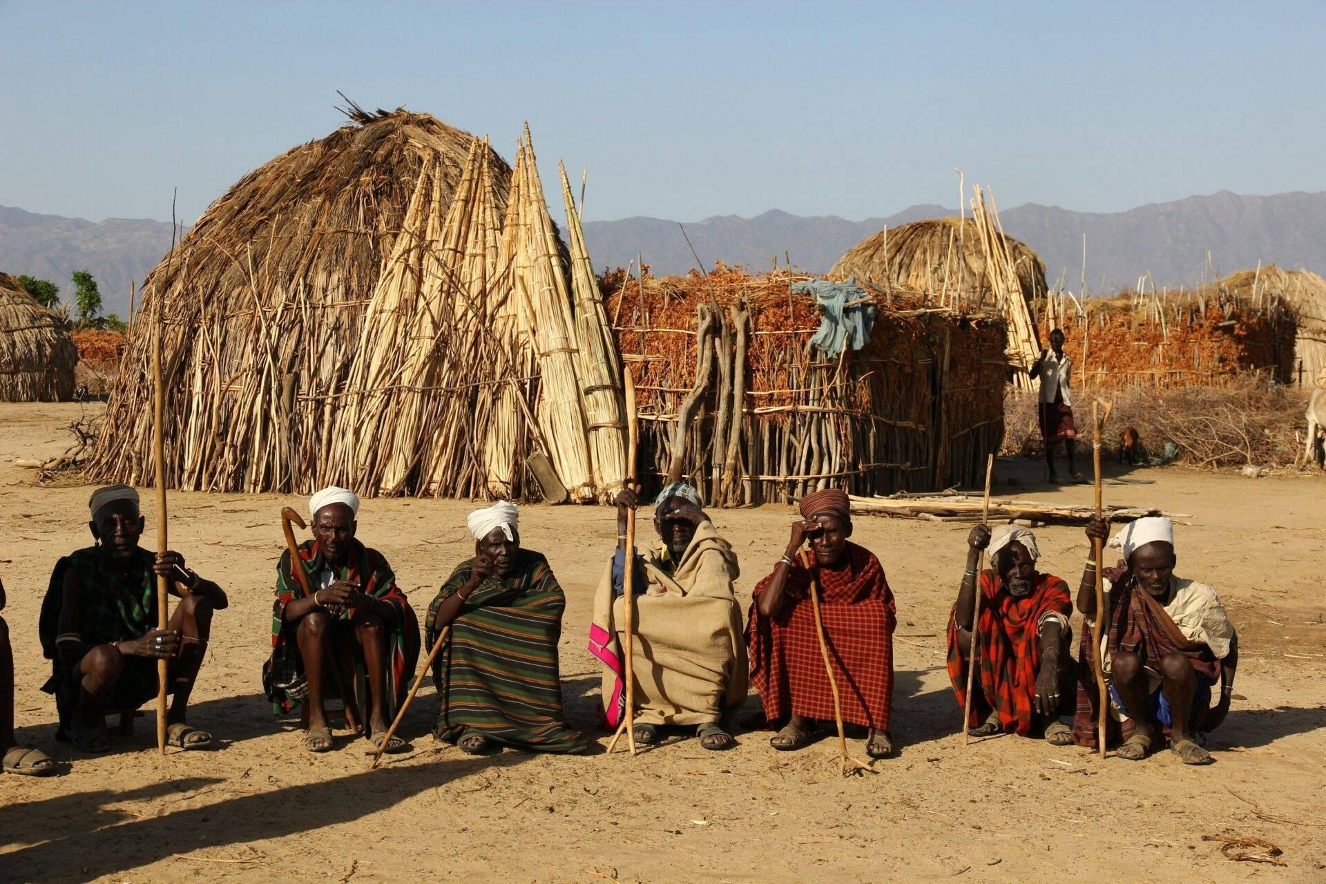 Group of Ethiopian warriors in colourful traditional dress posing in front of thatched huts in a pastoral village