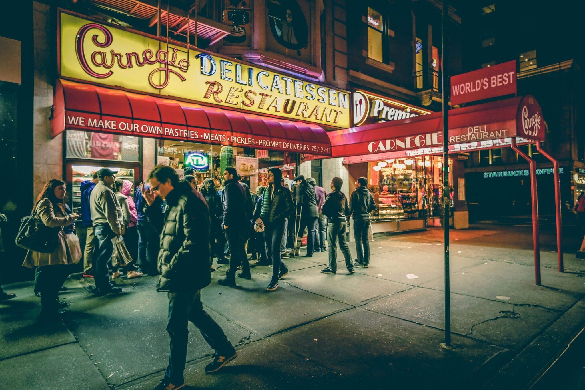 A lively shopping street at night with illuminated shopfronts and a crowd of pedestrians