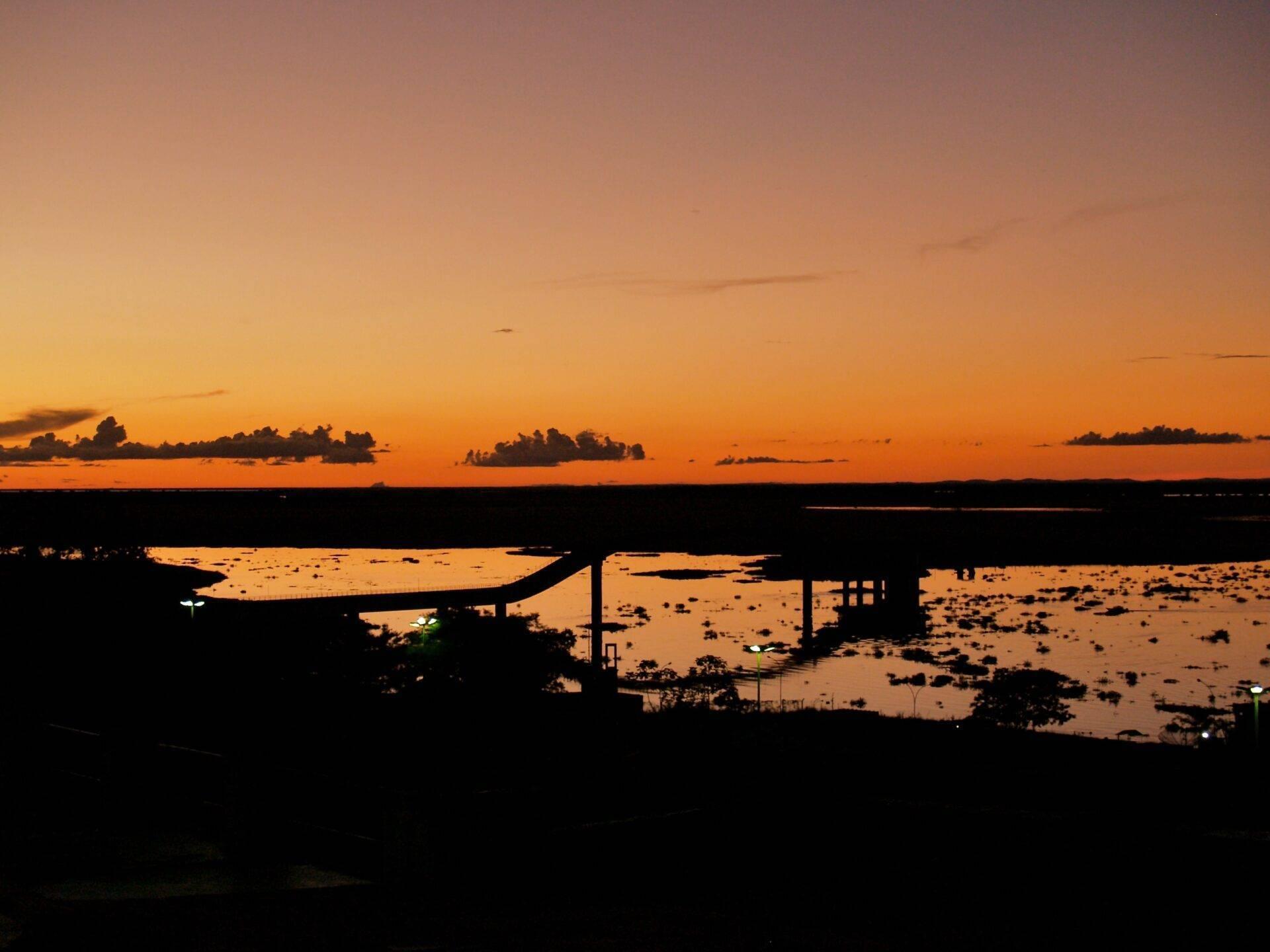 Tramonto dorato su un fiume con ponte stradale e zone allagate in silhouette