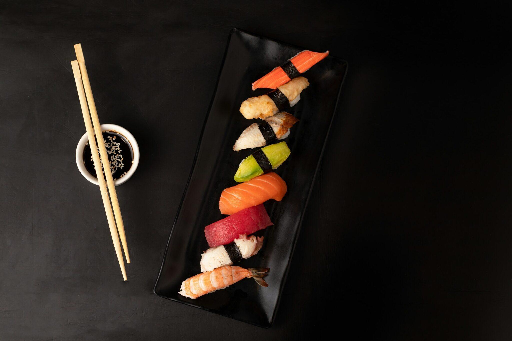 Surtido de nigiri sushi variados presentados en una bandeja negra con palillos y salsa de soja