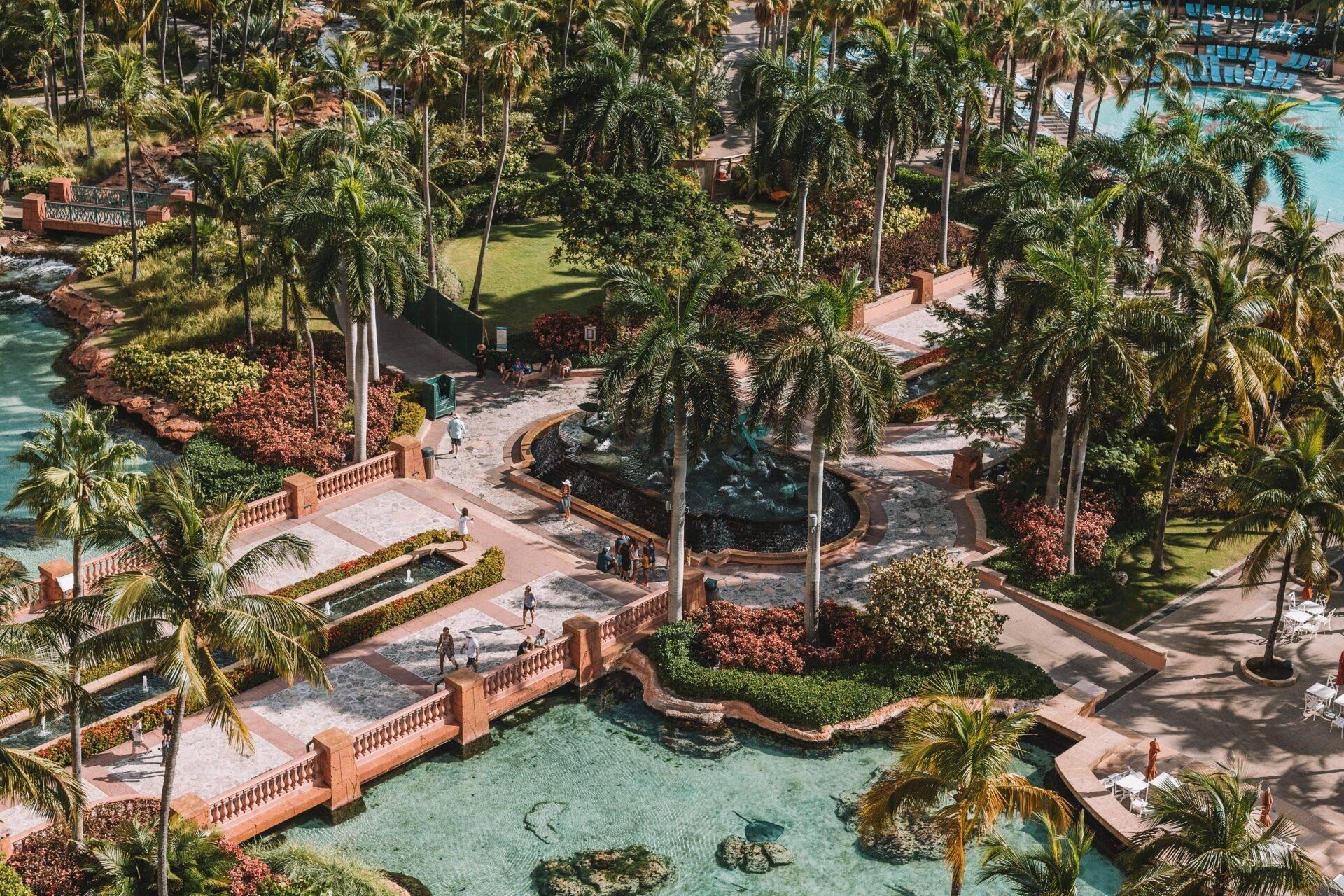 Aerial view of a tropical resort with turquoise pools, brick terraces, palm trees and sculptures set among lush greenery