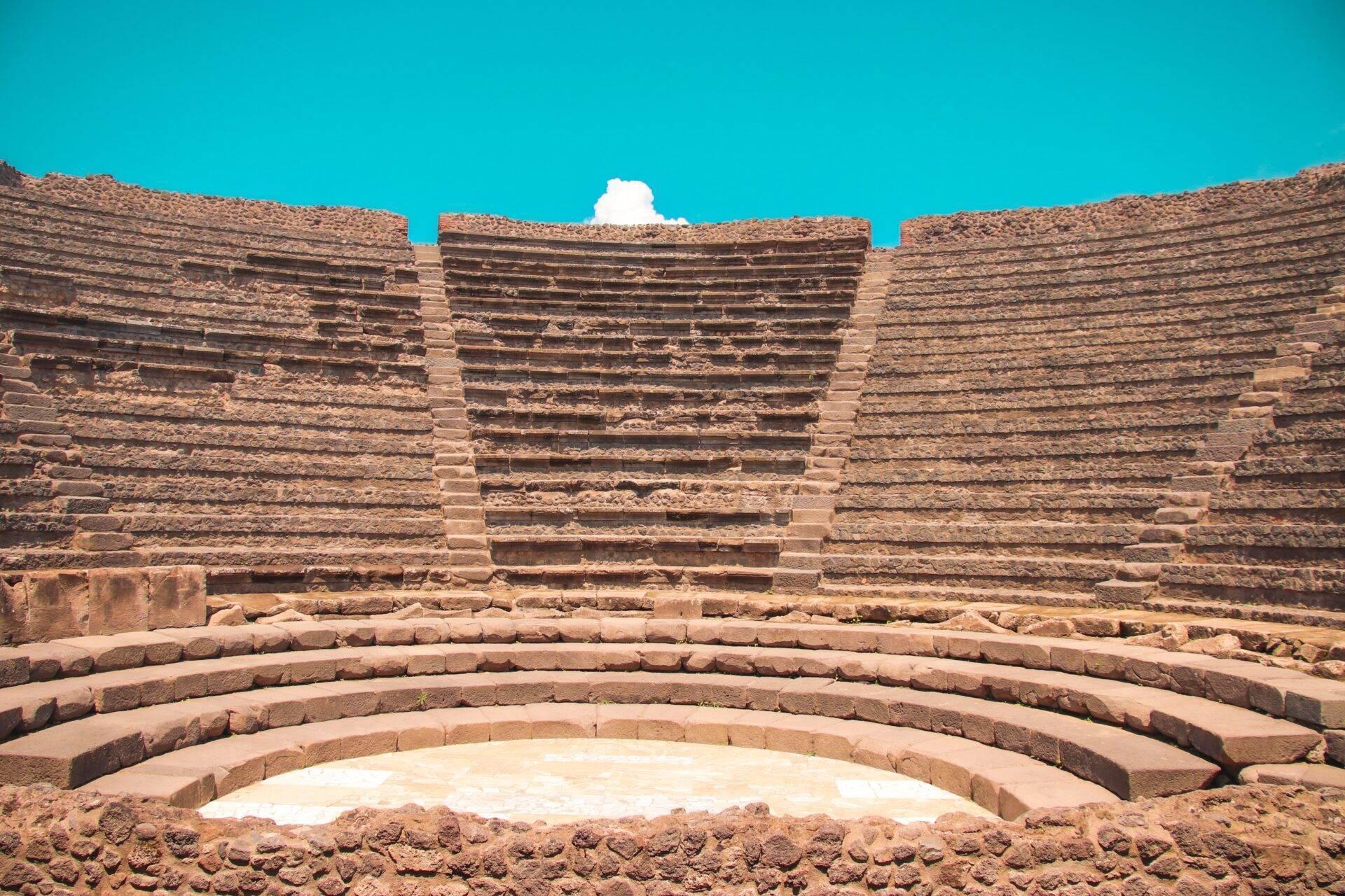 An ancient ruined amphitheatre with concentric stone seating tiers under a clear blue sky