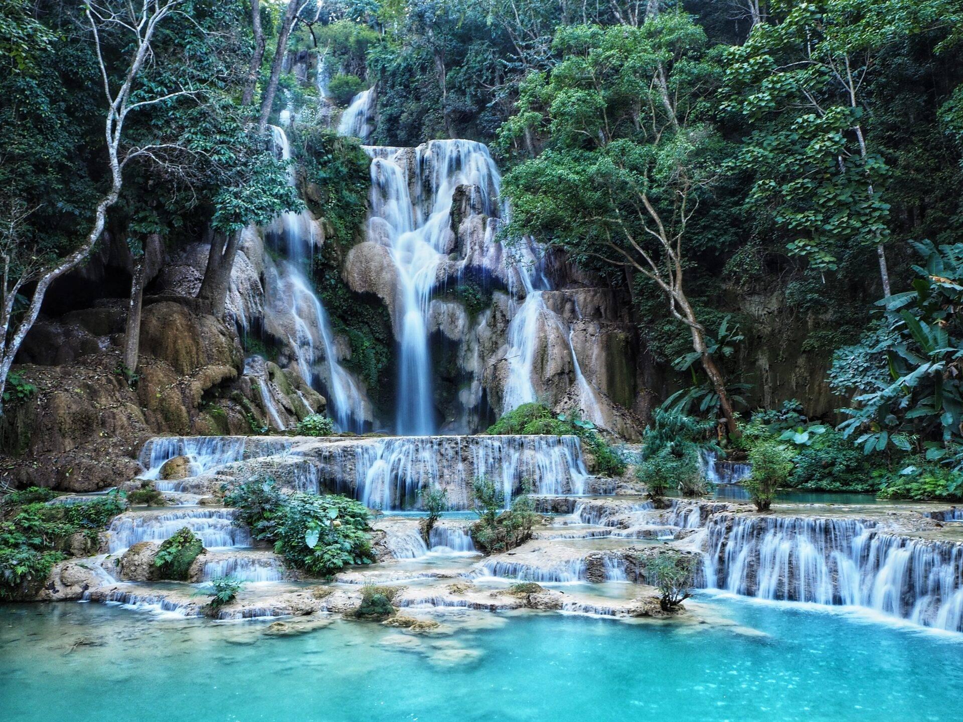 Una cascata a gradoni turchese che scorre in una lussureggiante foresta tropicale tra rocce e vegetazione