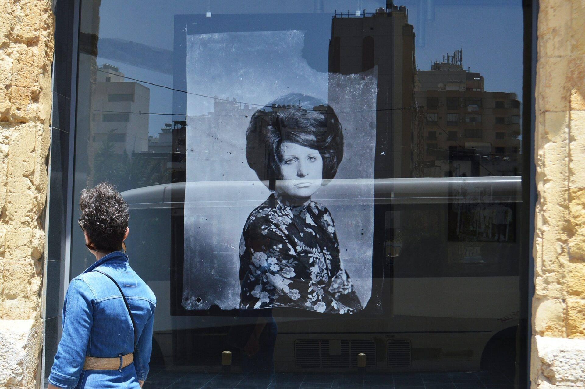Una mujer observa un retrato en blanco y negro de una mujer de los años 60 expuesto en un cristal en un entorno urbano