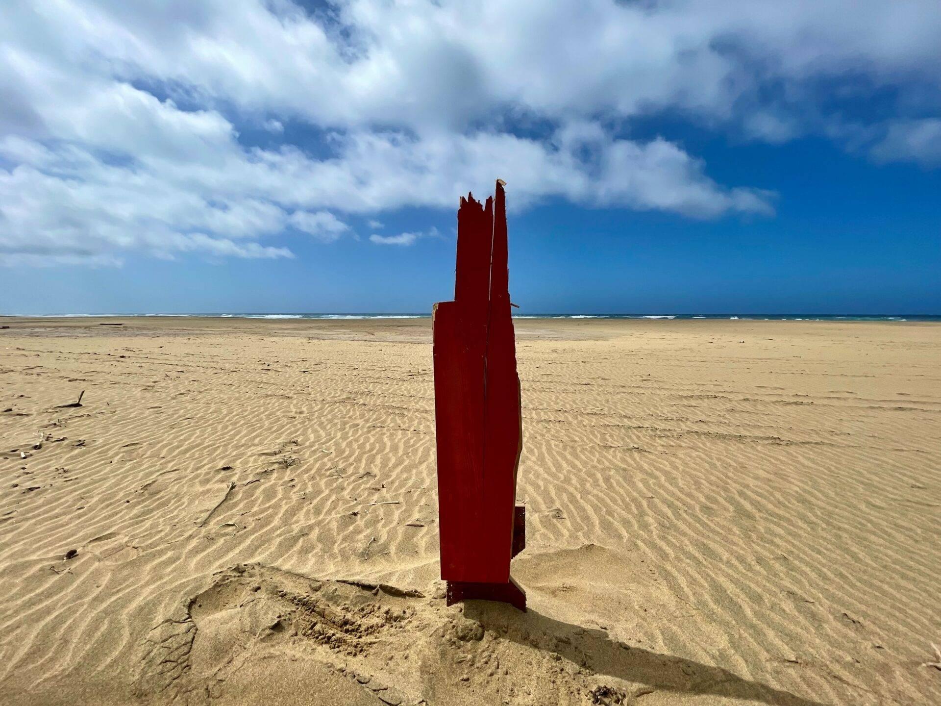 Una struttura metallica rossa arrugginita emerge dalla sabbia di una vasta spiaggia deserta alle Canarie sotto un cielo nuvoloso