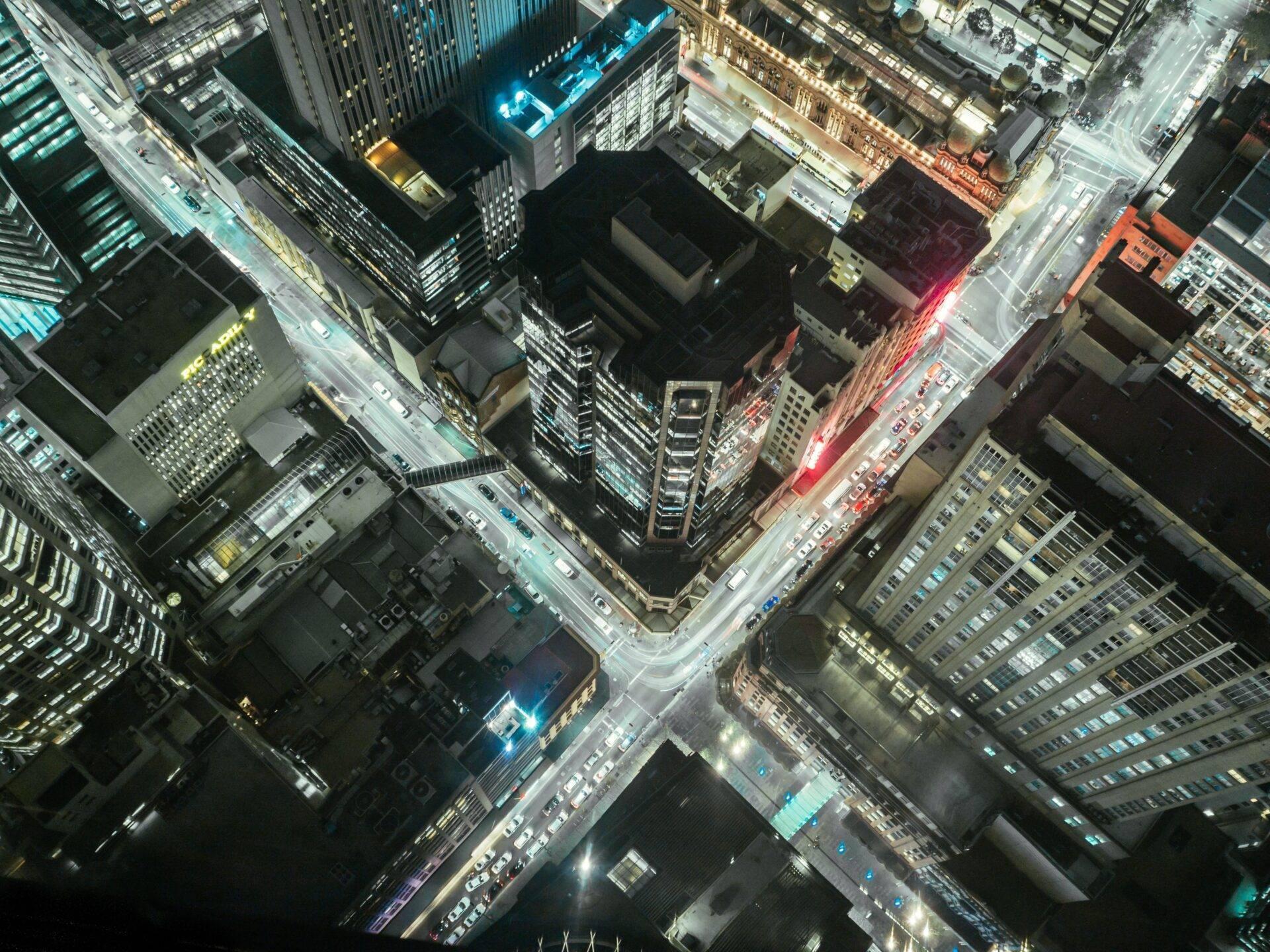 Vista aerea notturna di un’animata intersezione urbana con edifici illuminati e traffico stradale