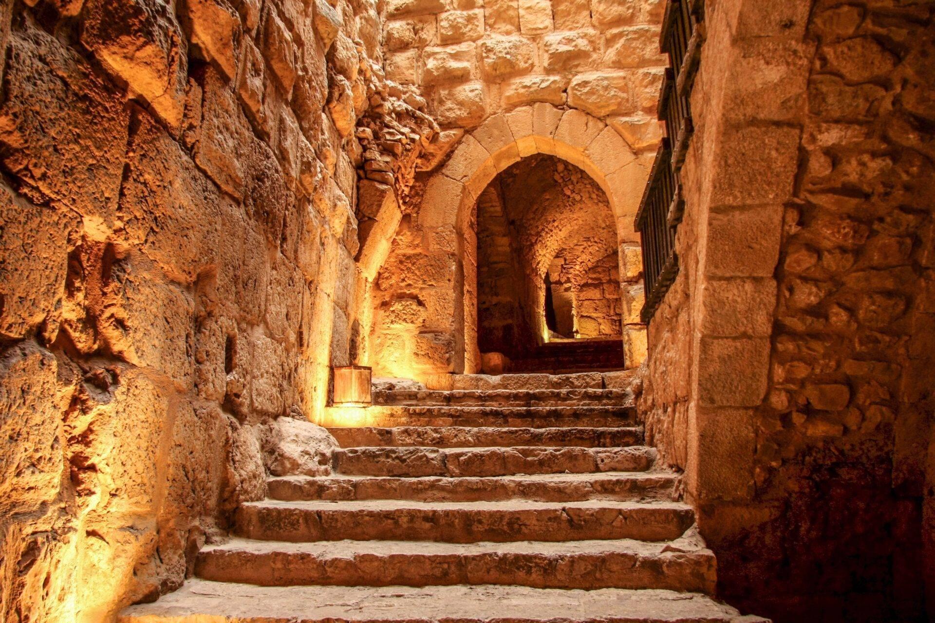 Escalera de piedra iluminada que conduce a un arco abovedado en una antigua fortaleza de Oriente Próximo