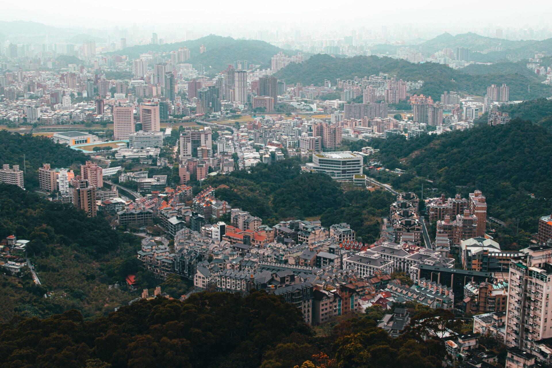 Vista aerea di una città montuosa densa con palazzi residenziali, verde circostante e nebbia atmosferica