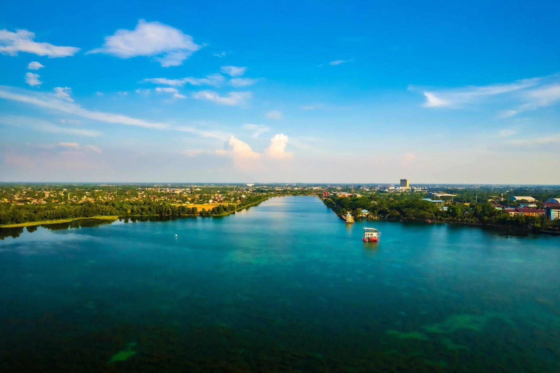 Vista aerea di un fiume turchese bordato da vegetazione tropicale con un’imbarcazione turistica e una città costiera