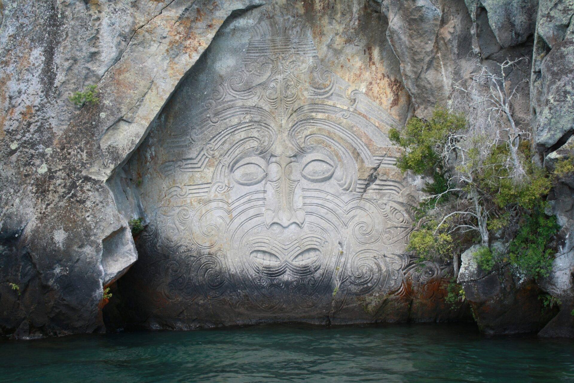 Intaglio maori scolpito nella roccia che sovrasta un’acqua turchese in Nuova Zelanda