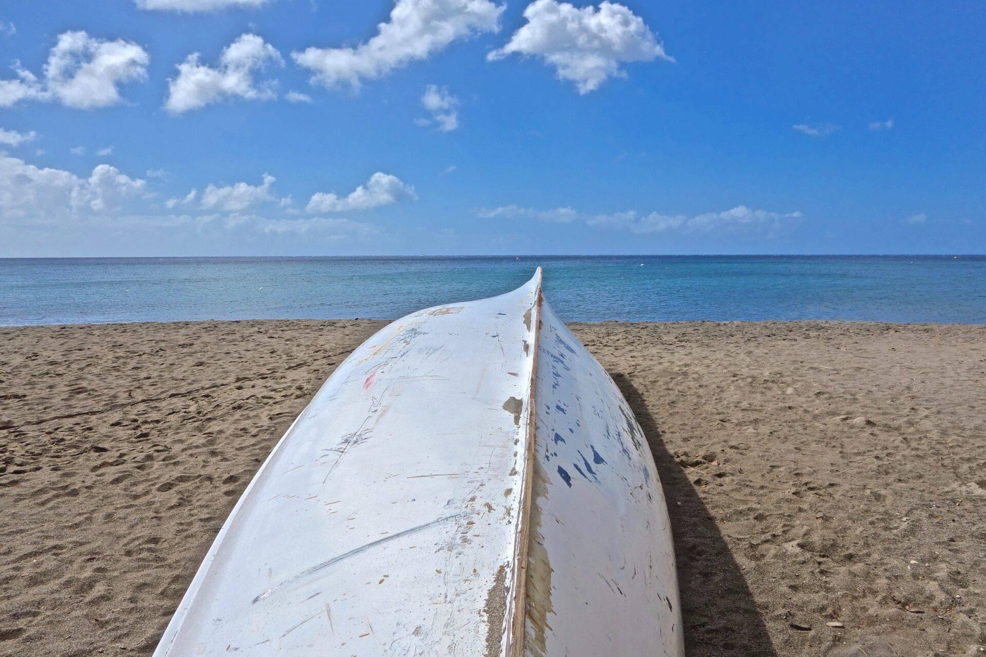 Ein altes weißes Boot liegt auf einem Feinsandstrand vor türkisfarbenem Meer unter blauem Himmel