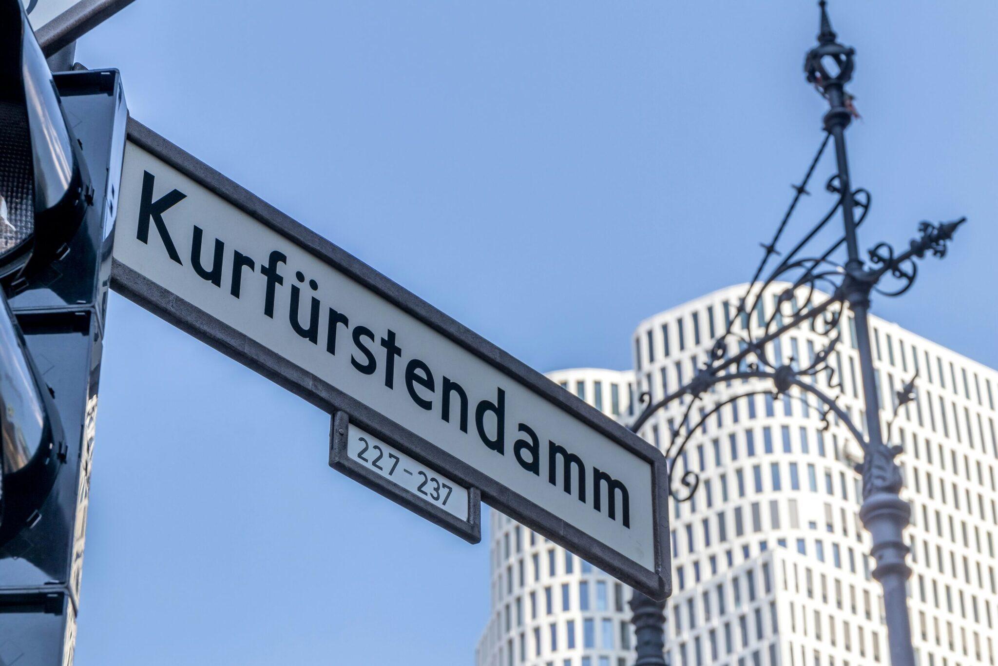 Placa de la calle Kurfürstendamm con los números 227-237 y edificios modernos berlineses al fondo bajo un cielo azul
