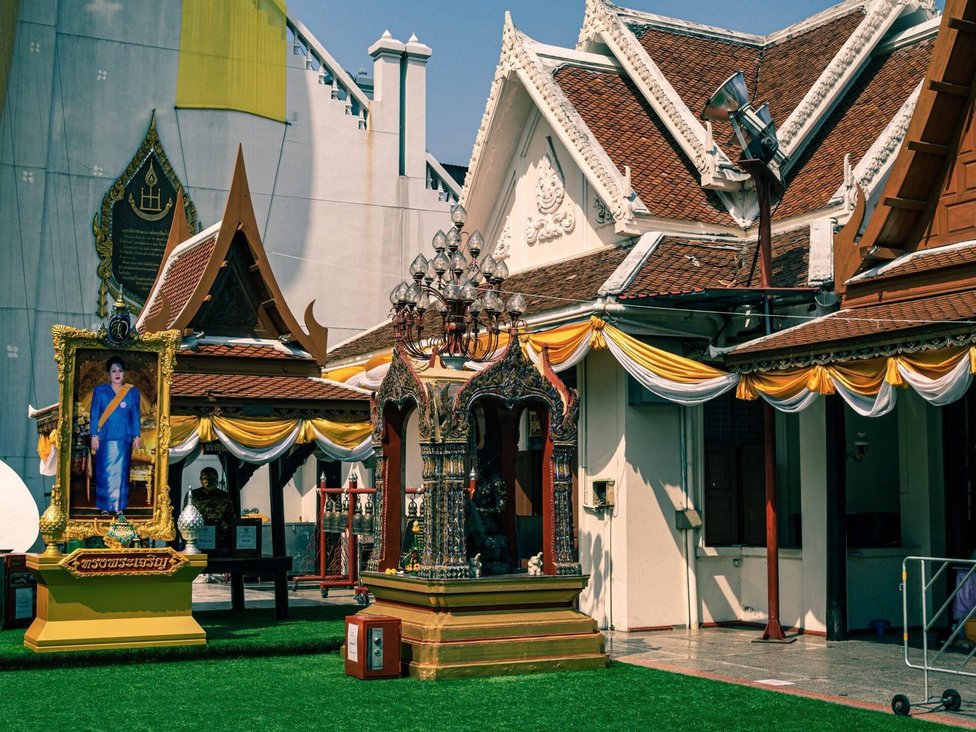Un tempio buddista thailandese con tetti dorati decorati con bandiere gialle e bianche sotto un cielo azzurro soleggiato