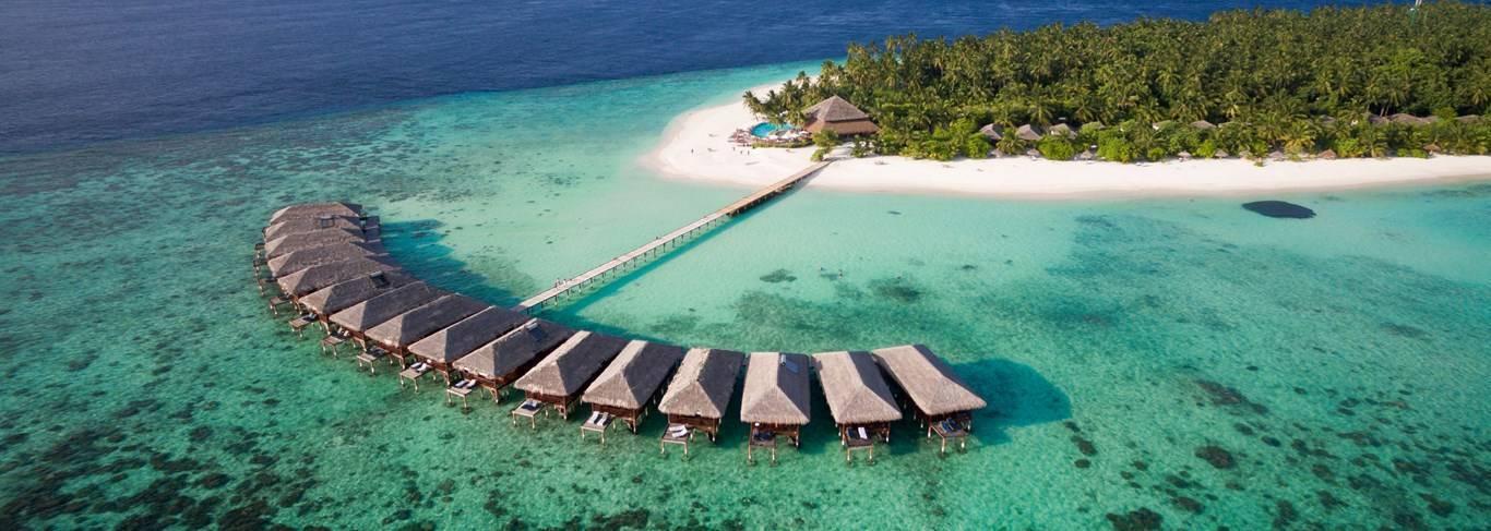 Vista aerea di un resort tropicale con bungalow sull’acqua, spiaggia bianca e laguna turchese alle Maldive