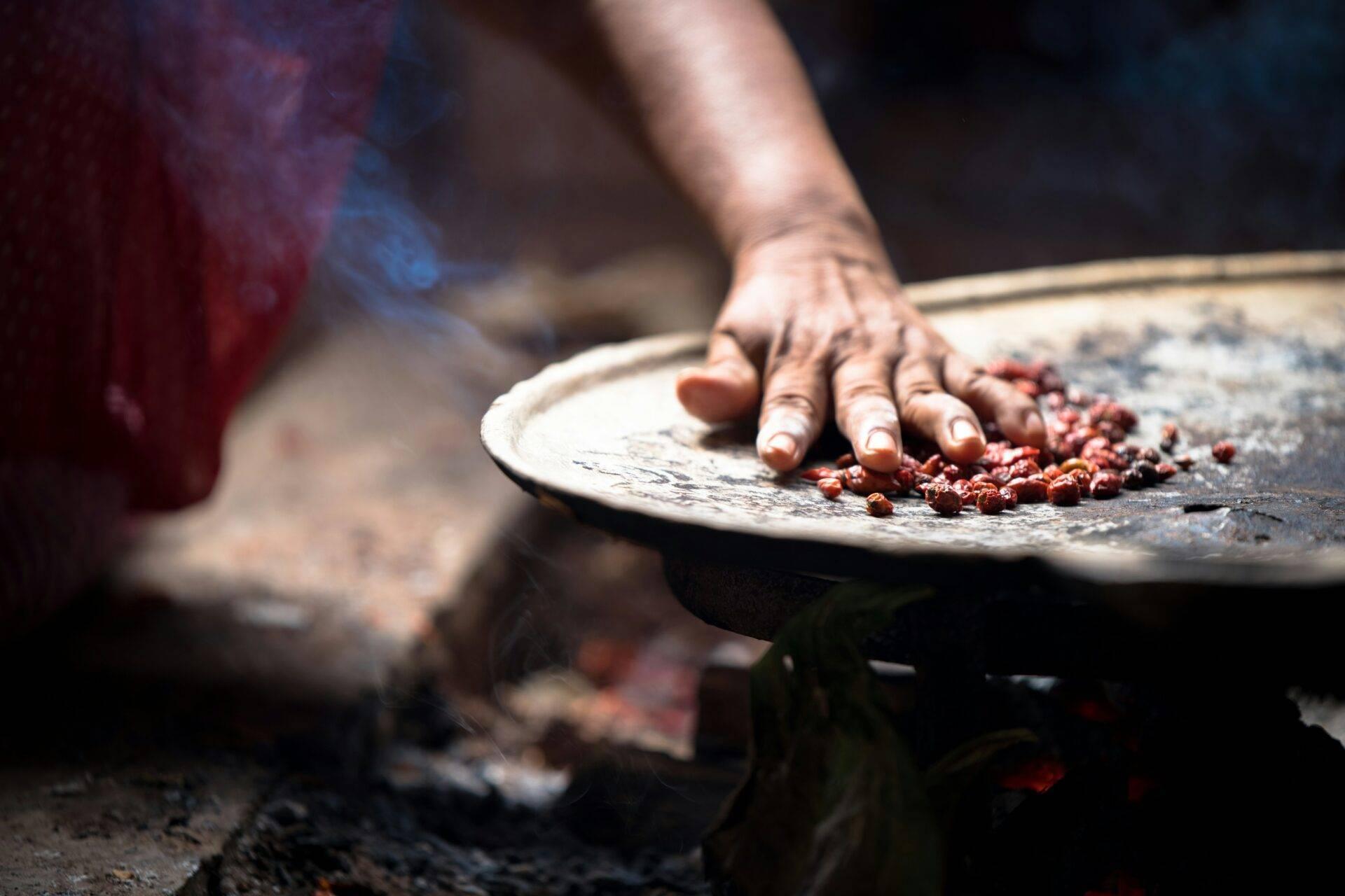 Eine Hand, die rote Kakaobohnen auf einer traditionellen flachen Unterlage in Guatemala mahlt
