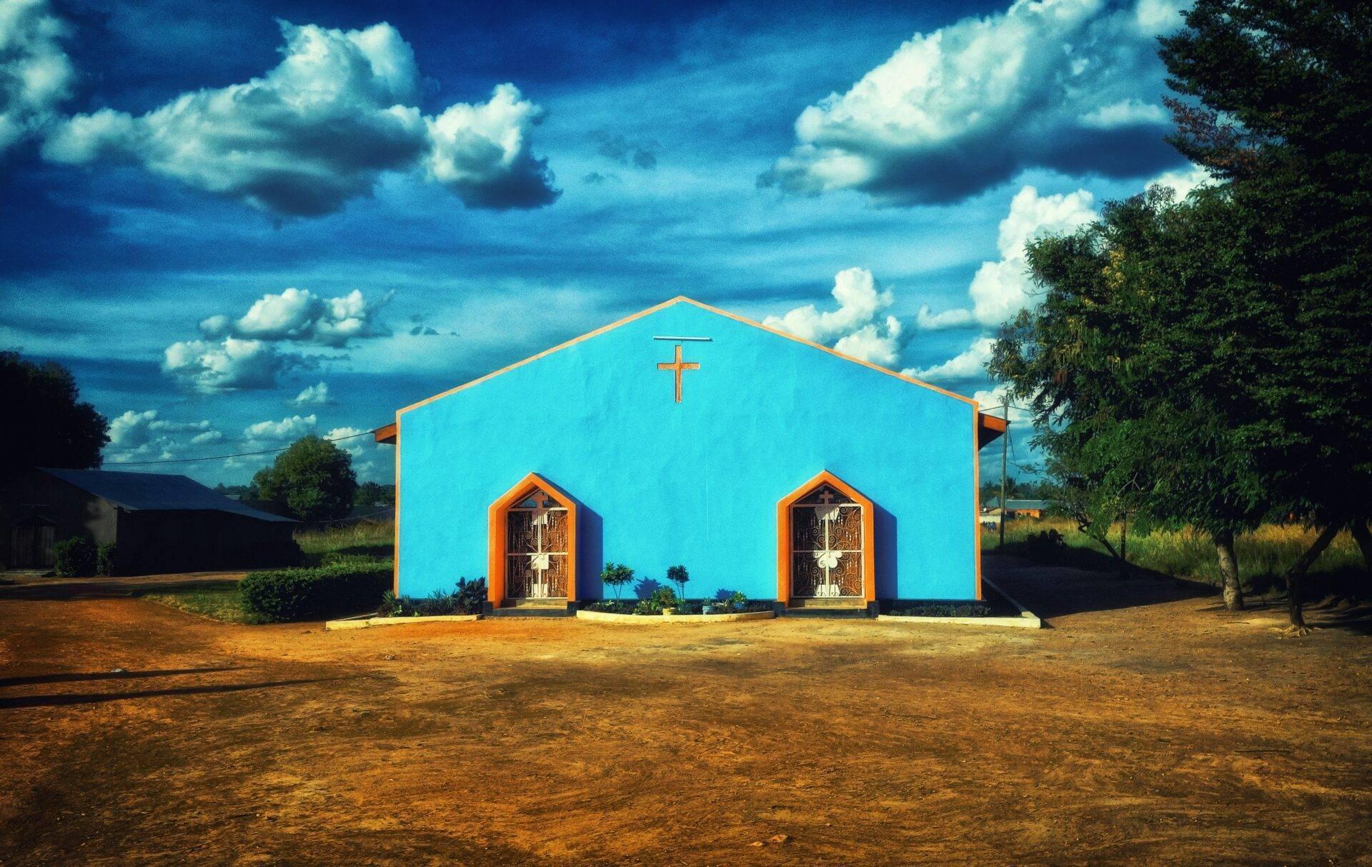 A church with vivid blue walls and orange doors in an African savanna under a cloudy sky